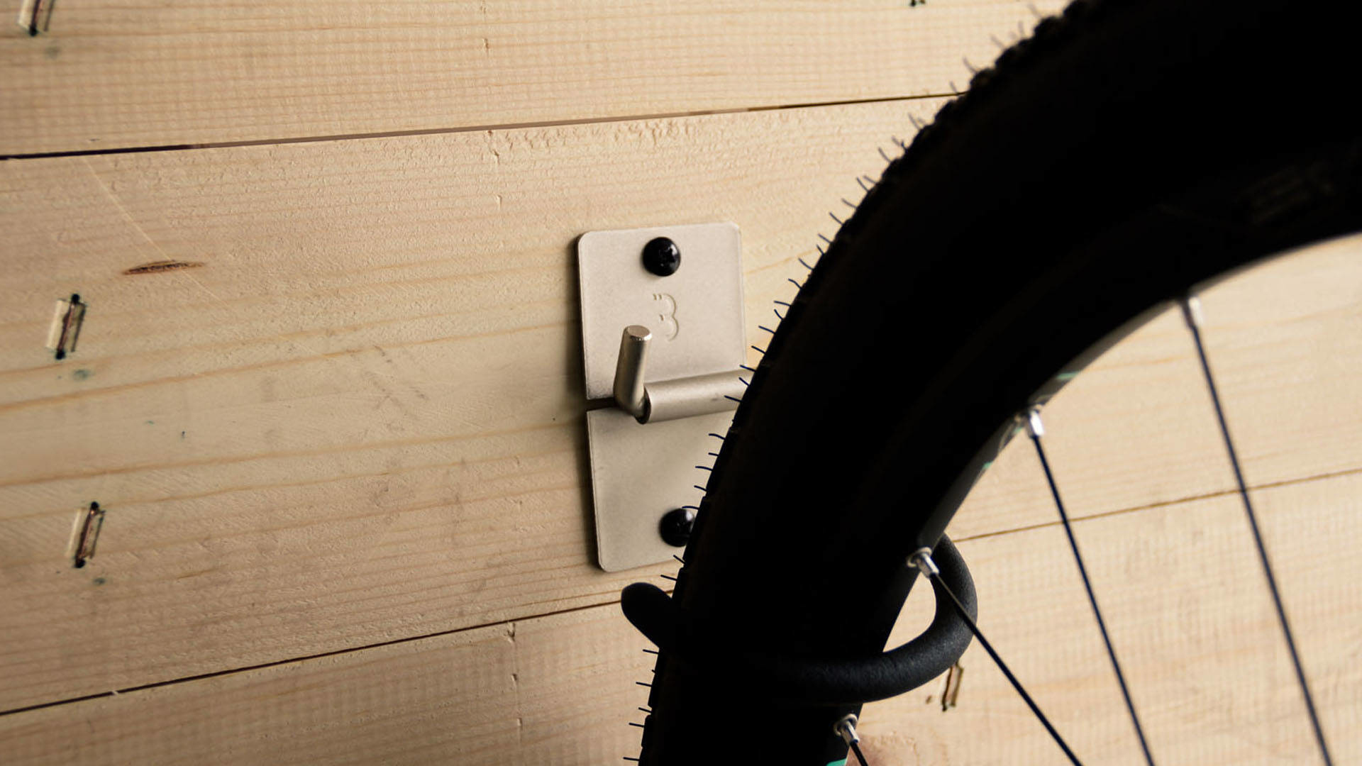 Koło rowerowe wisi na zamontowanym na ścianie metalowym haku przymocowanym do drewnianych desek.