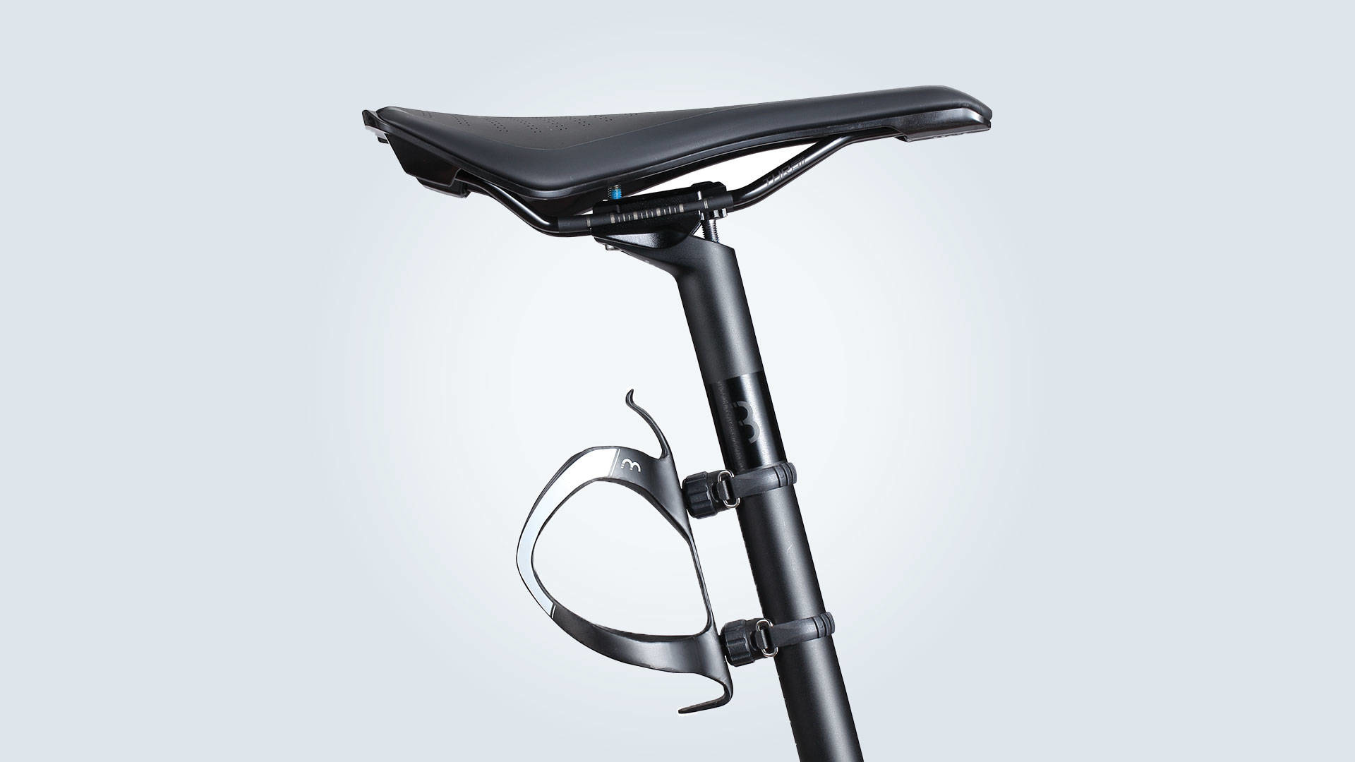 Siodło i sztyca rowerowa z dołączonym koszykiem na bidon. Tło jest jasnoniebieskie.