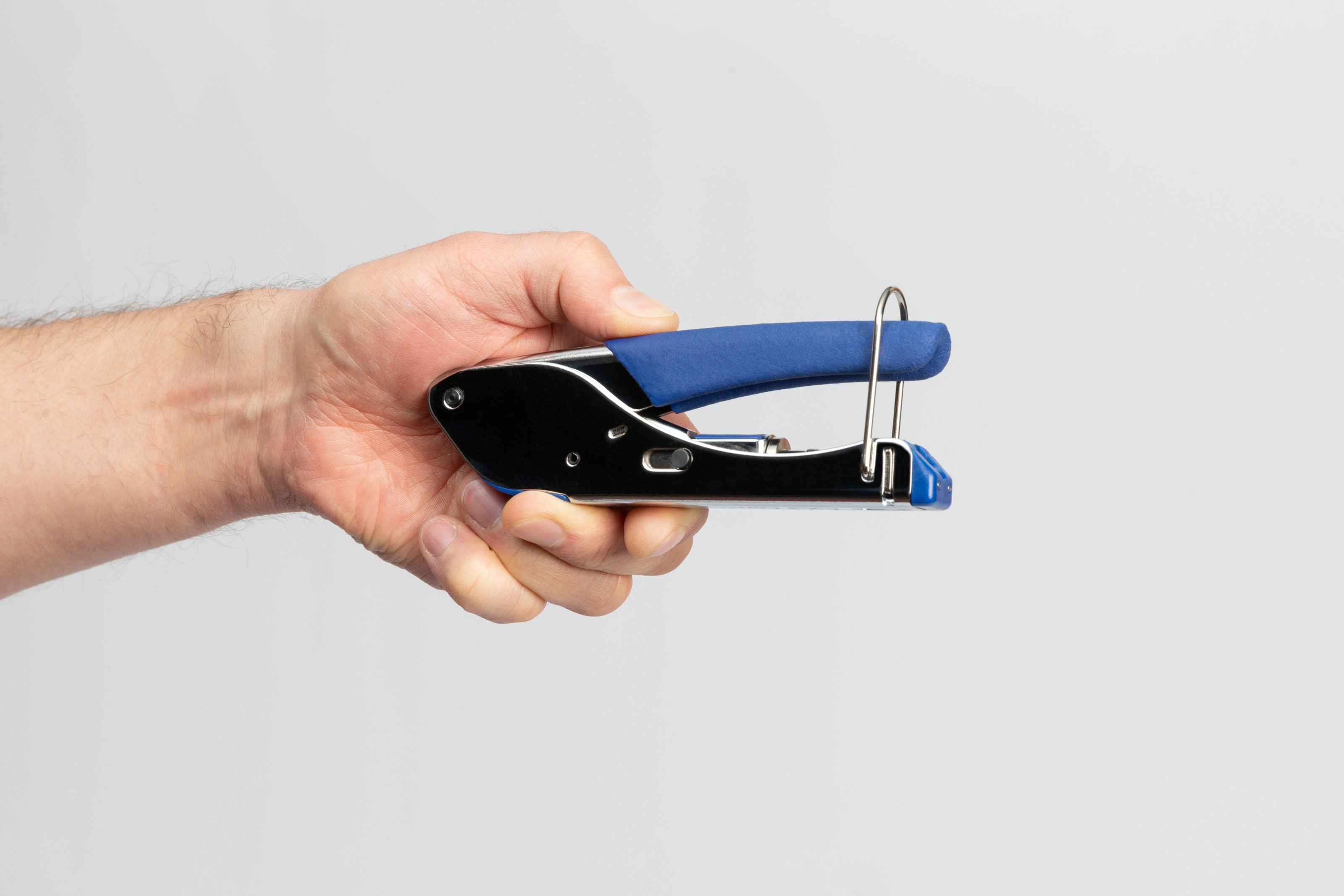 Ręka trzymająca zaciskarkę z niebieskim uchwytem i srebrnym korpusem.
