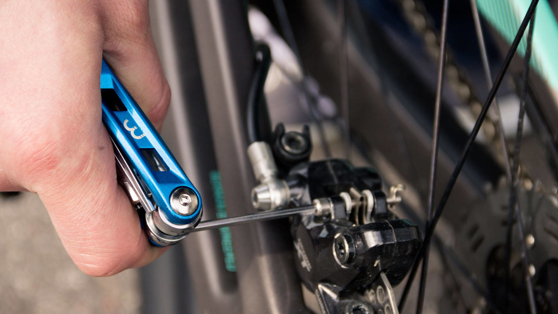Osoba używa niebieskiego multi-toola do regulacji hamulca rowerowego. Hamulec jest czarny.