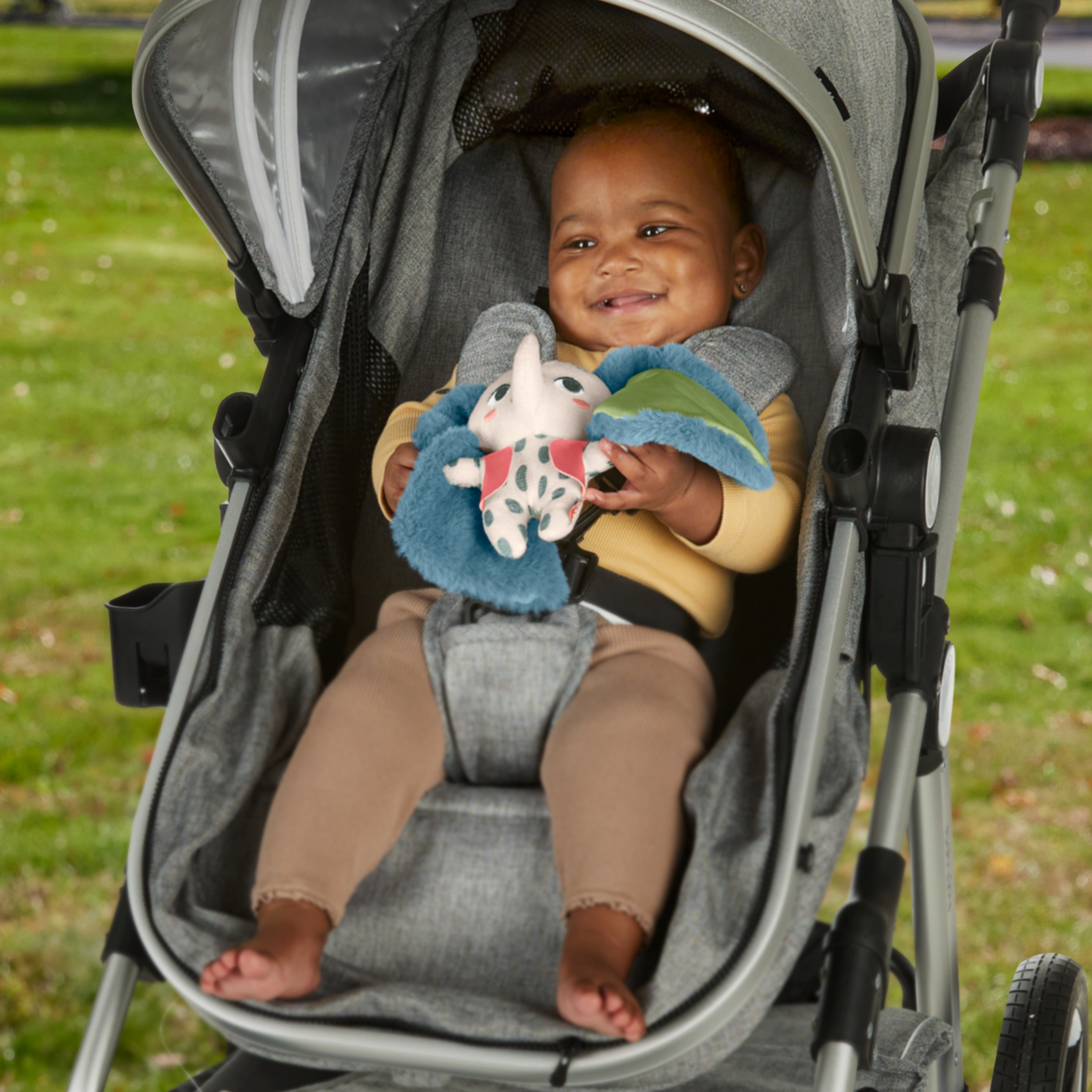 Dziecko w wózku uśmiecha się, trzymając pluszową zabawkę słonia.