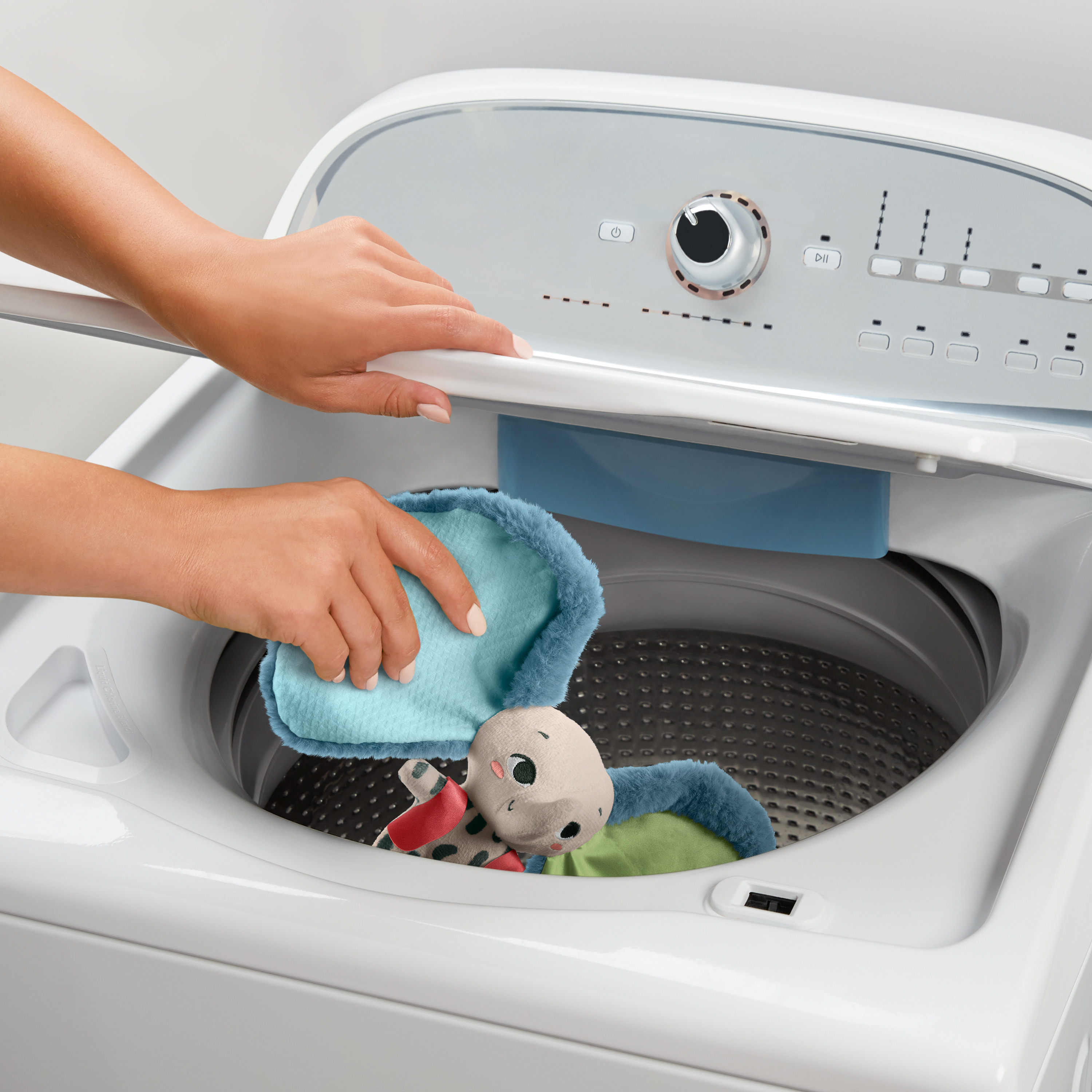 Osoba pierze pluszową zabawkę w białej pralce.