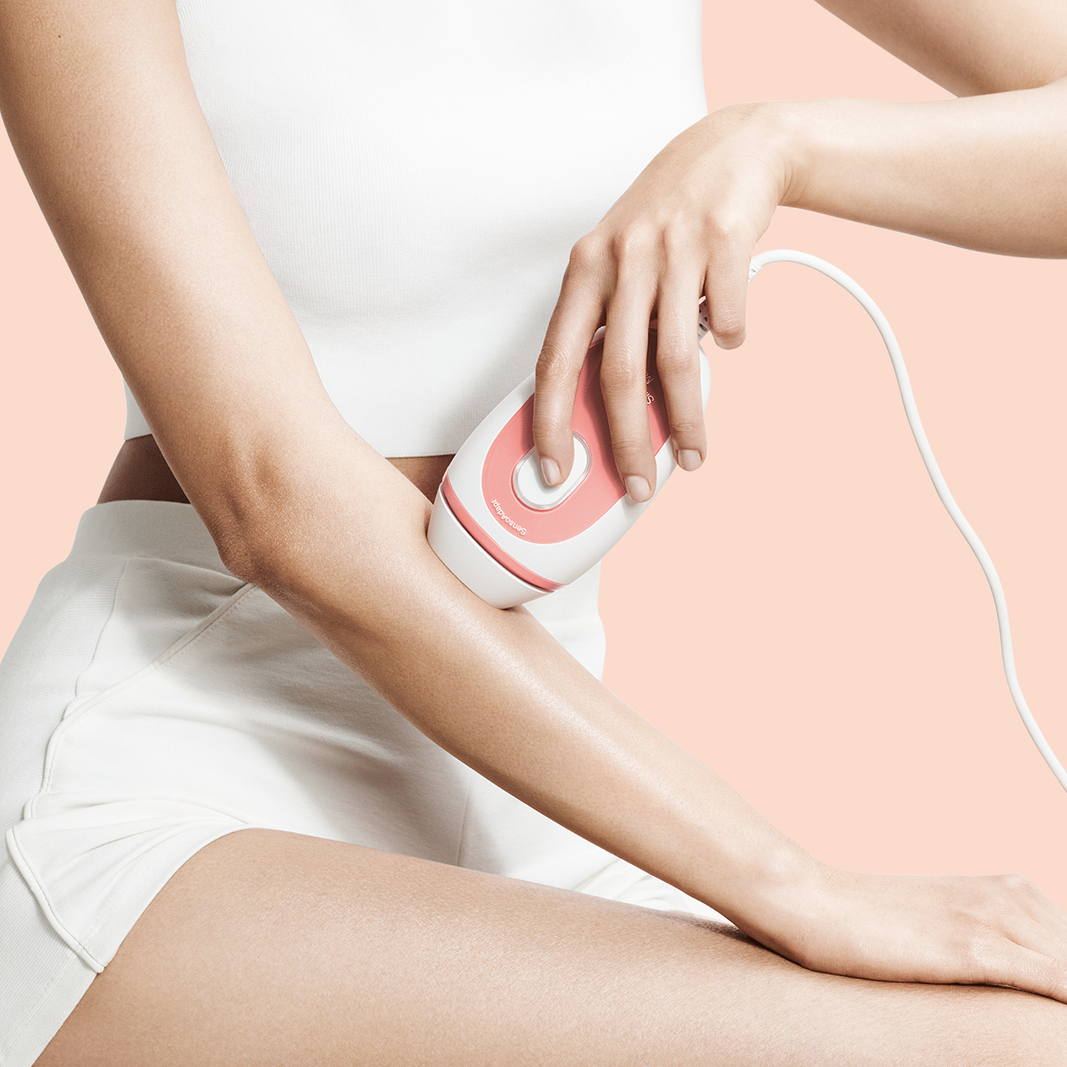 Bir kişi pembe ve beyaz bir Braun Silk-expert Mini IPL cihazını kolunda kullanıyor. Arka plan şeftali rengi.
