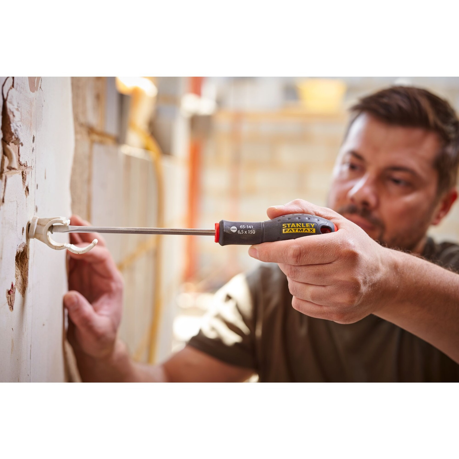 Mężczyzna używający śrubokręta Stanley FatMax do wkręcania czegoś w ścianę.