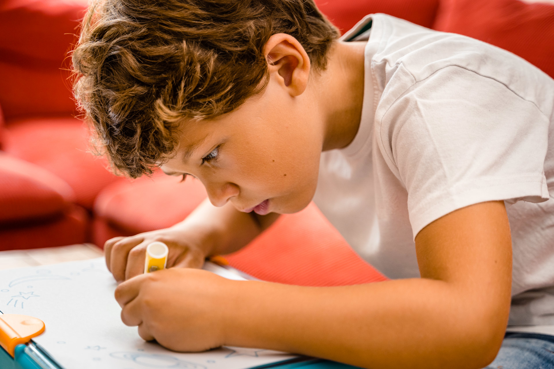 Chłopiec rysuje na białej kartce żółtym markerem, skupiona twarz.