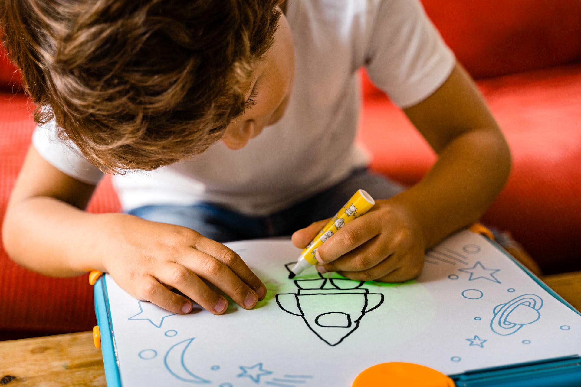 Chłopiec rysuje rakietę żółtym markerem na białej tablicy.