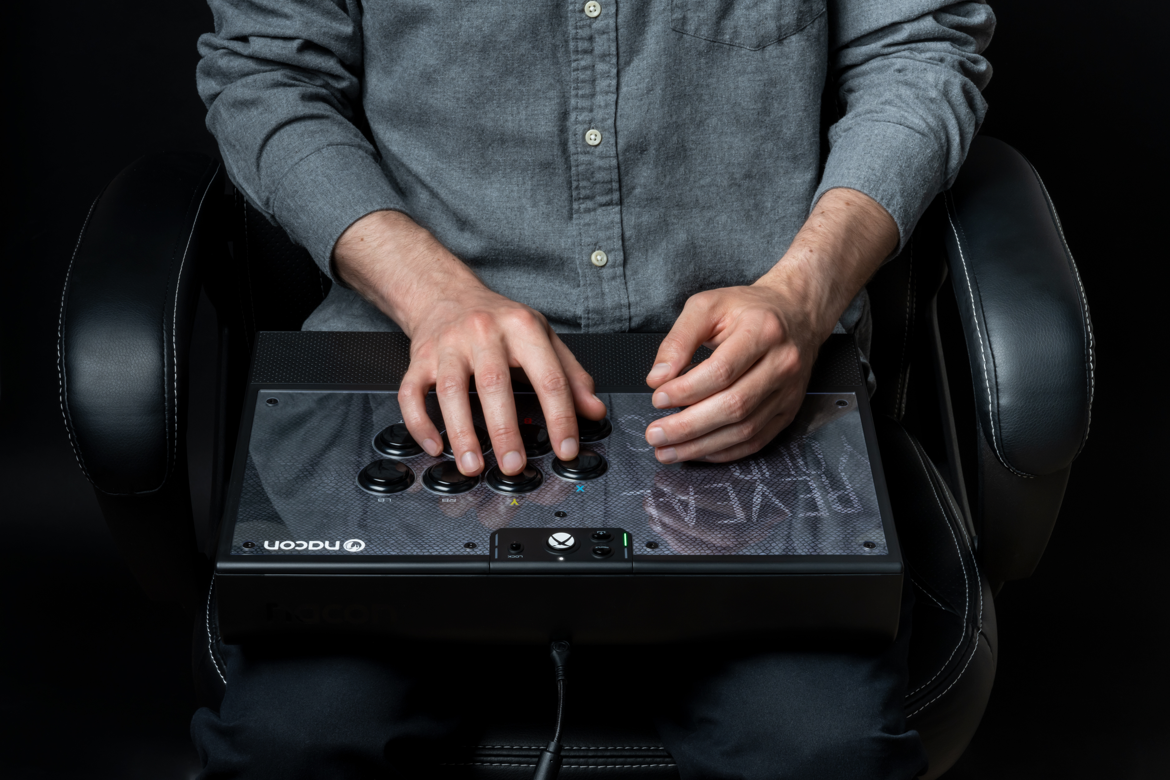 Osoba siedząca na krześle, trzymająca kontroler z przyciskami.