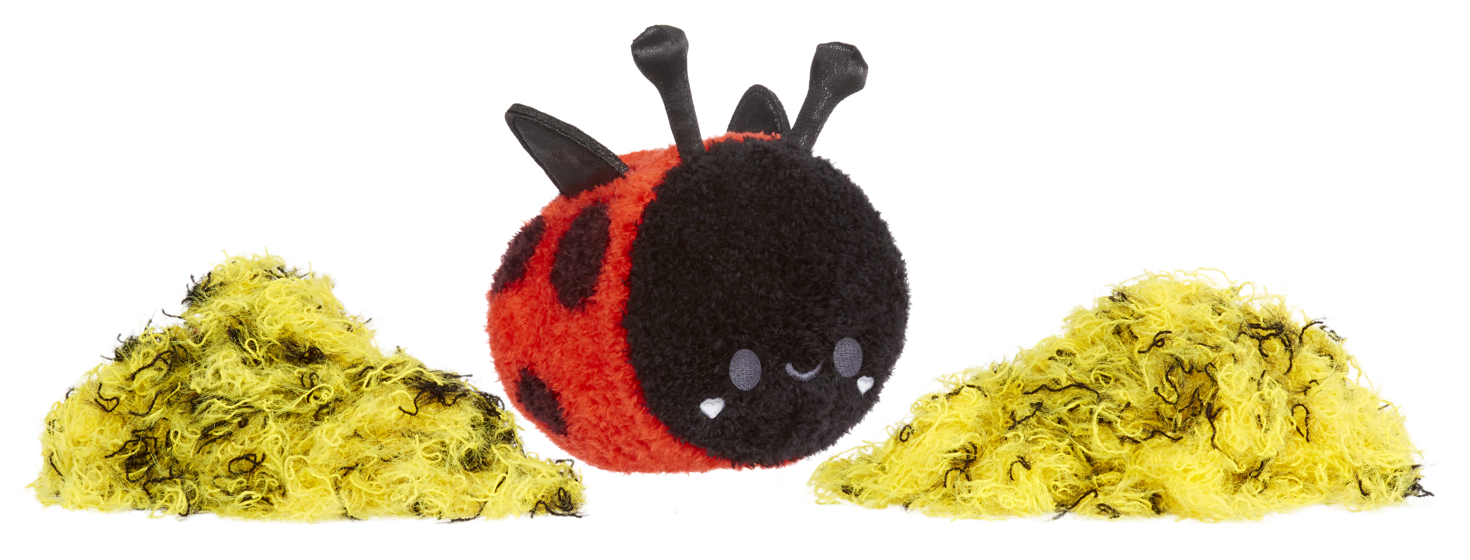 Un giocattolo a forma di coccinella di peluche, rosso con pois neri, tra due mucchi di materiale giallo sminuzzato.