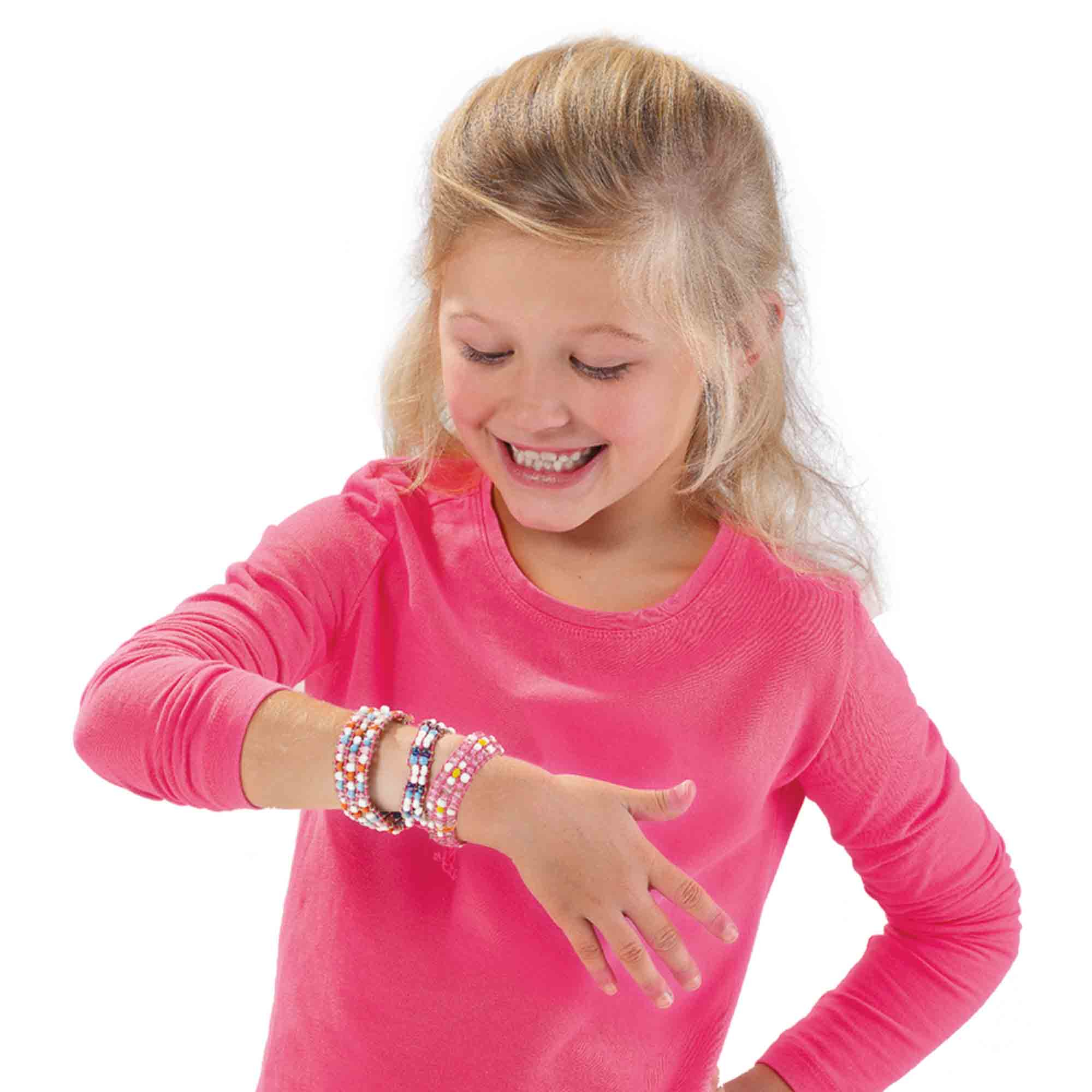 Dziewczyna uśmiecha się, pokazując kilka bransoletek na nadgarstkach.