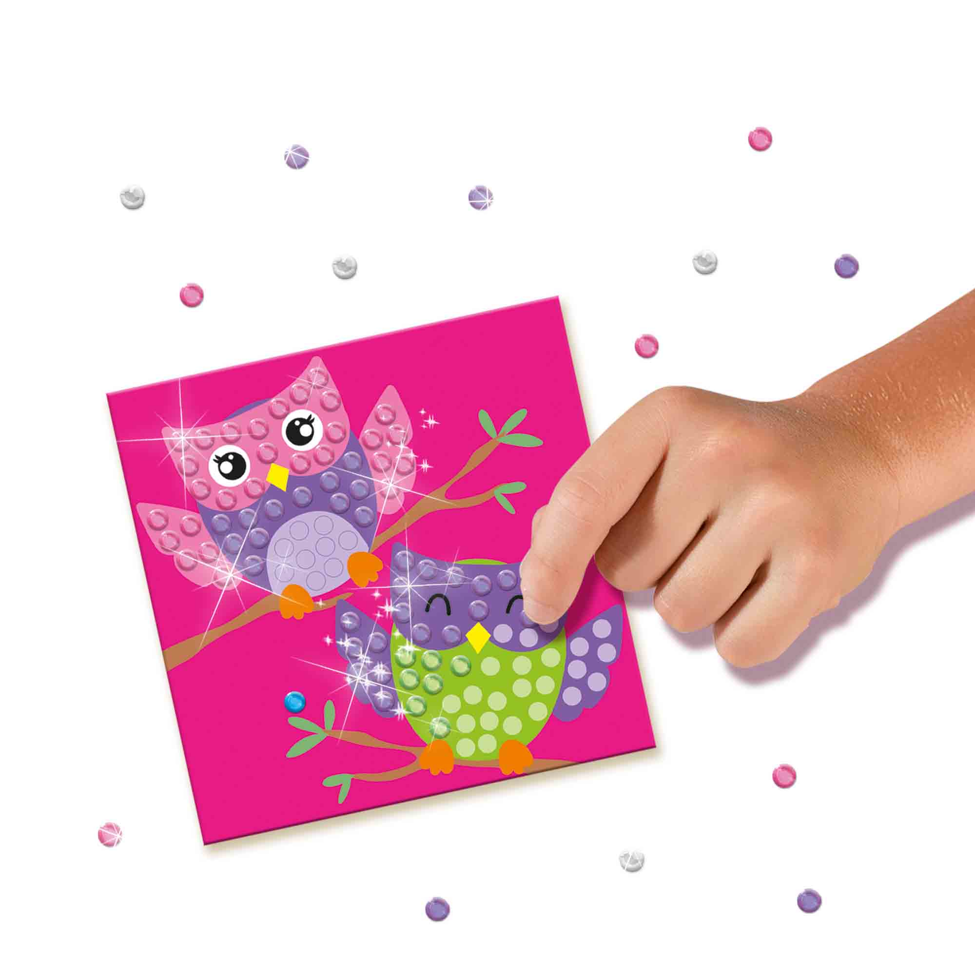 Ręka dziecka nakłada kropki na różową ilustrację sów na gałęzi, z cekinami dookoła.