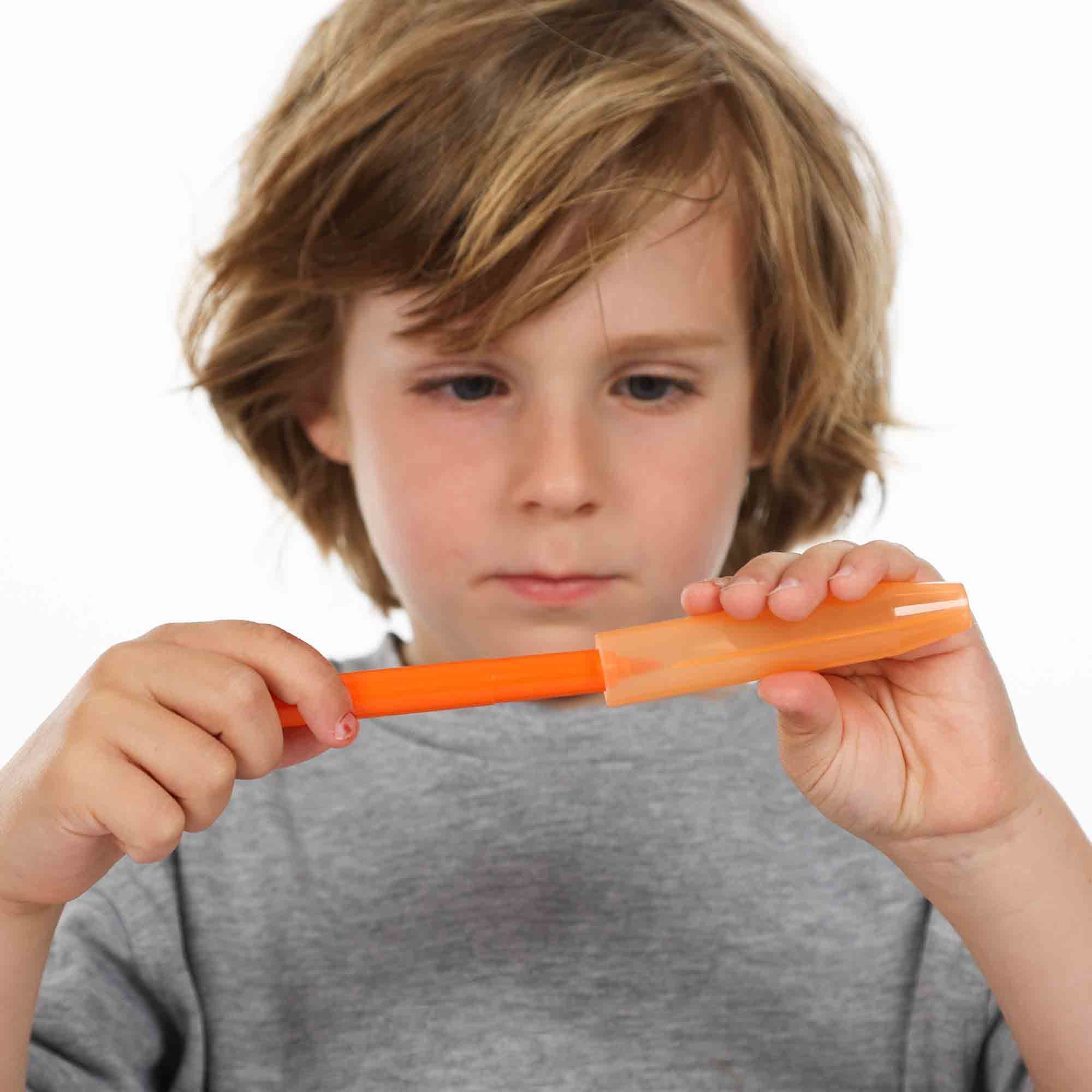 Chłopiec trzyma pomarańczową kredkę. Kredka w przezroczystym uchwycie. Białe tło, skupienie na dłoniach.