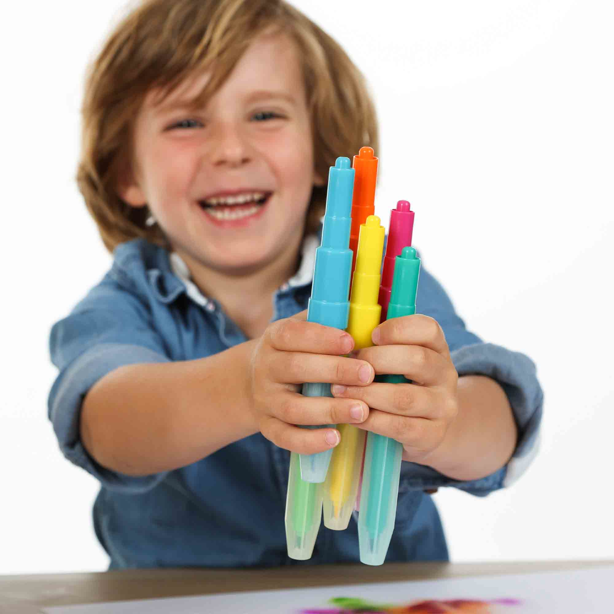 Chłopiec trzymający kolorowe markery, uśmiechnięty i patrzący w kamerę, na białym tle.