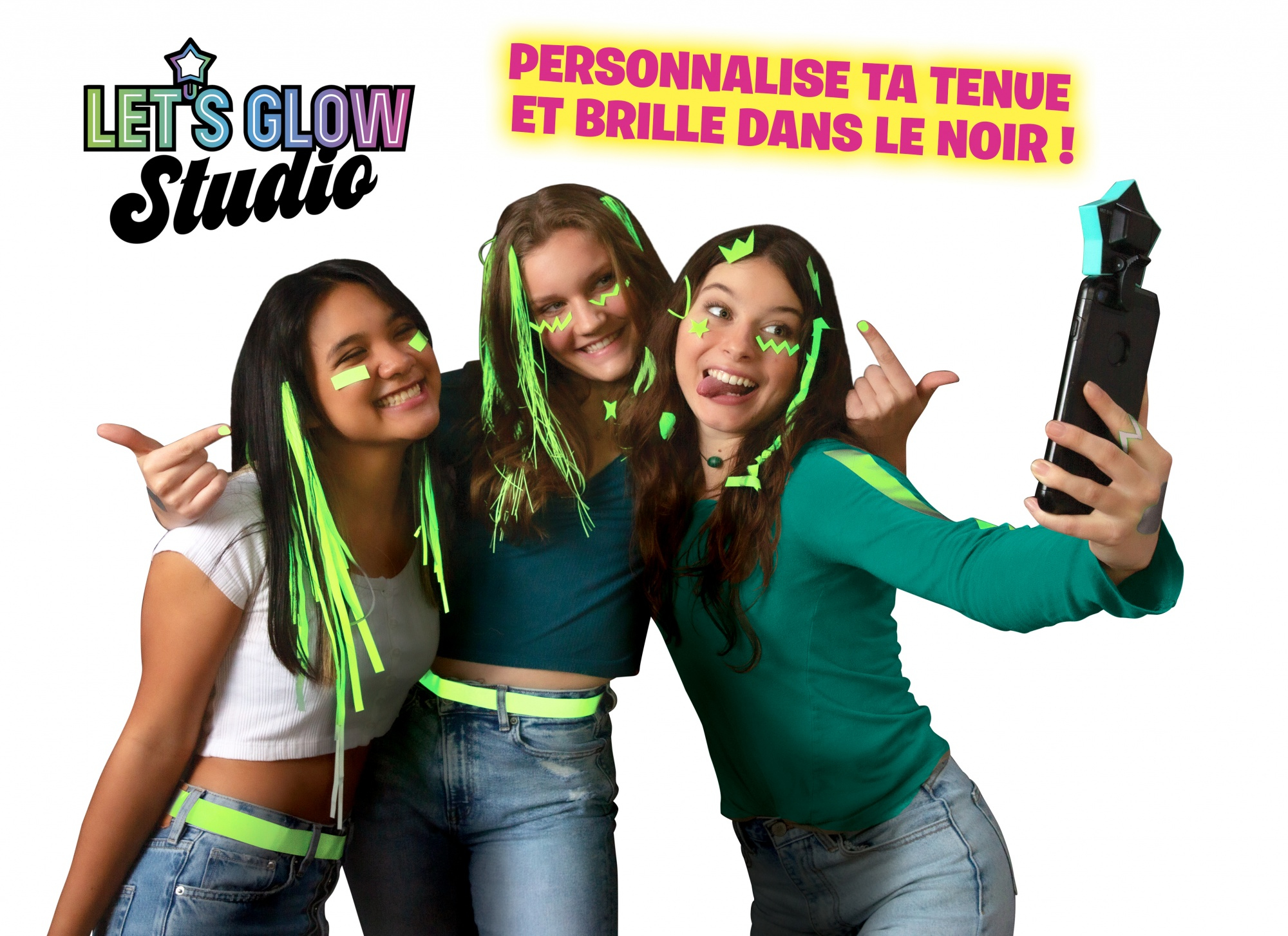Trzy dziewczyny pozują, nosząc neonowo-zielone akcesoria do włosów i ubrania, z kijem do selfie.