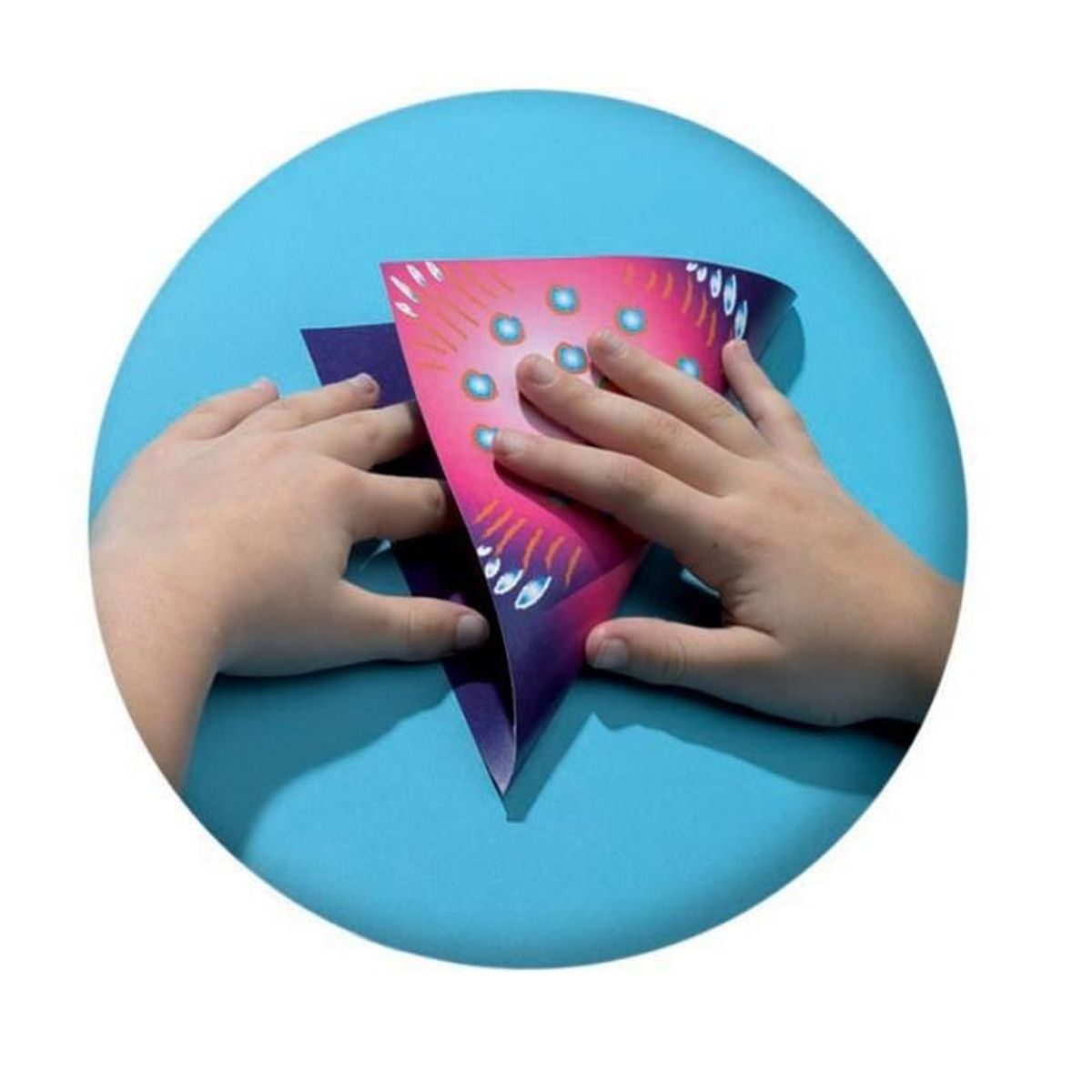 Ręce składają różowy papier, tworząc kształt stożka. Papier ma wzór kropek i linii.