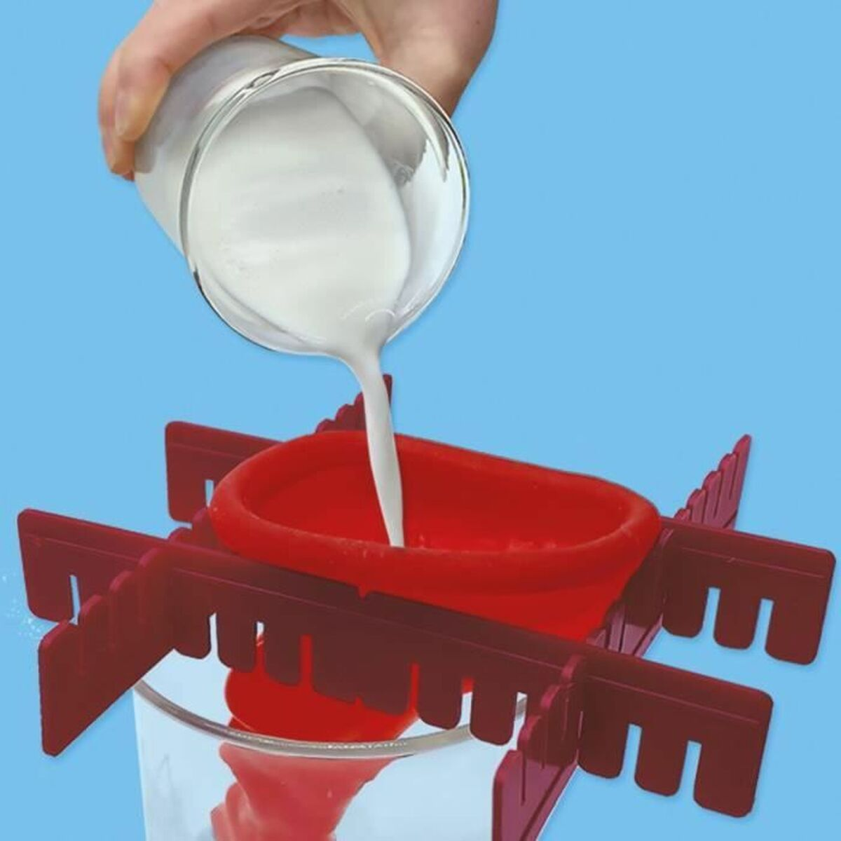 Mano versa liquido bianco in un imbuto rosso, tenuto da un telaio di plastica, su blu.