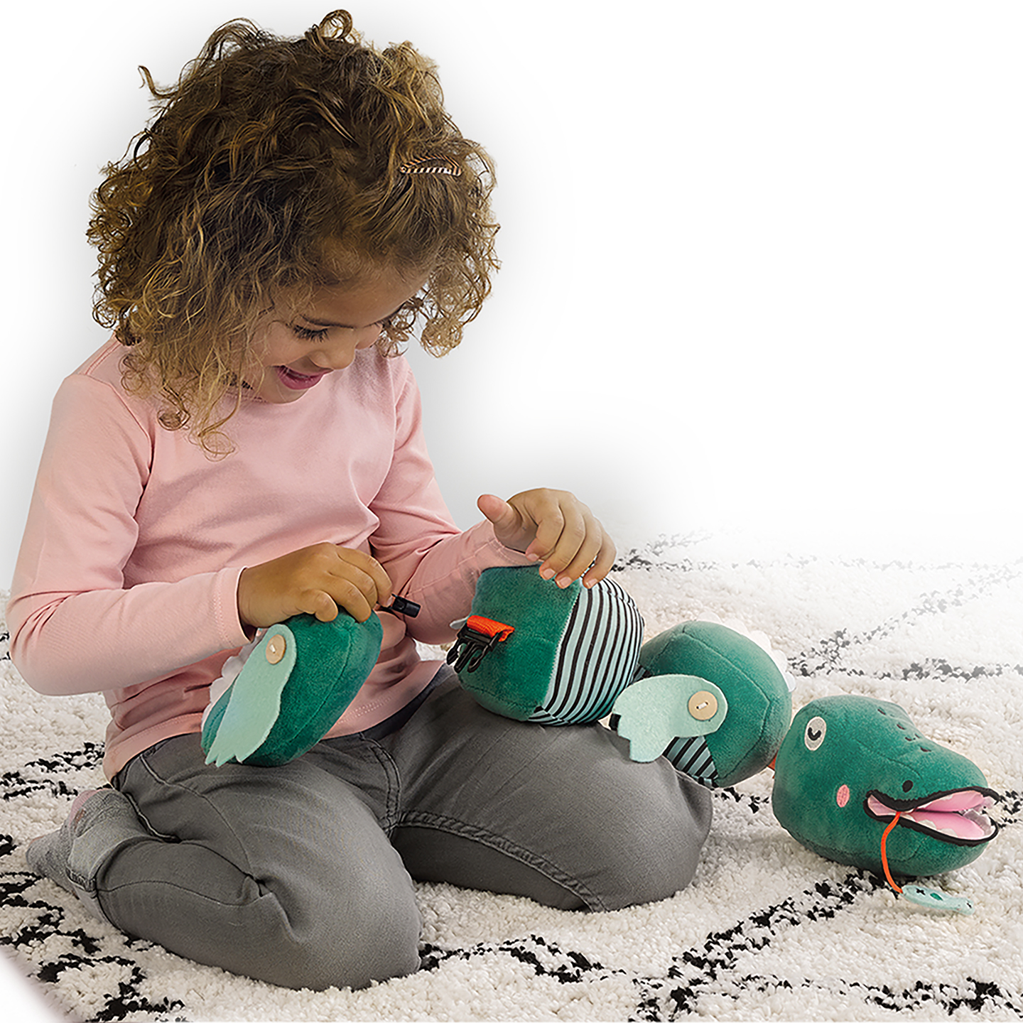 Una bambina gioca con giocattoli di coccodrillo di peluche su un tappeto.