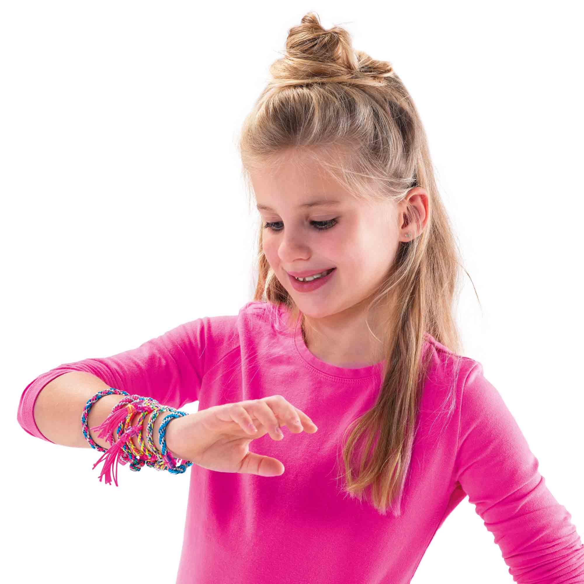 Dziewczyna w różowej koszuli patrzy na plecione bransoletki przyjaźni na nadgarstku. Bransoletki są kolorowe z frędzlami.