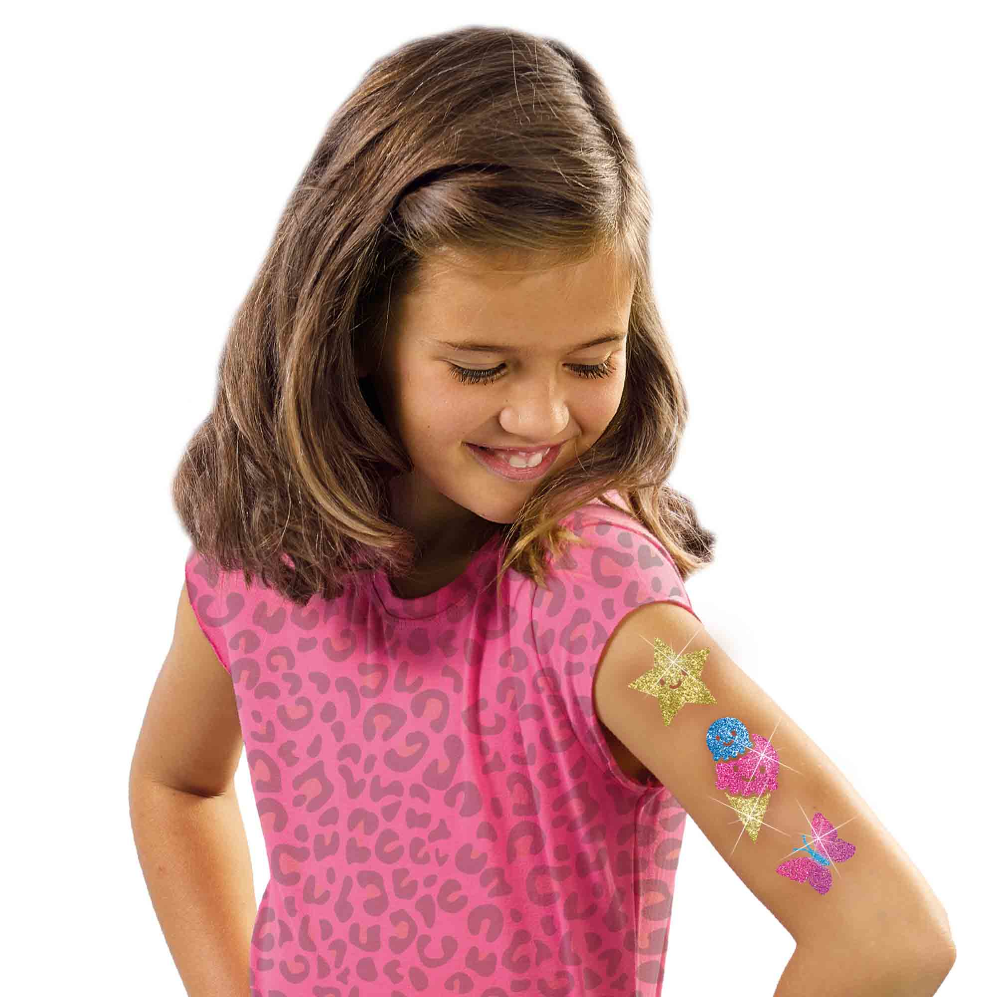 Dziewczyna z brokatowymi tatuażami na ramieniu uśmiecha się, patrząc w dół.