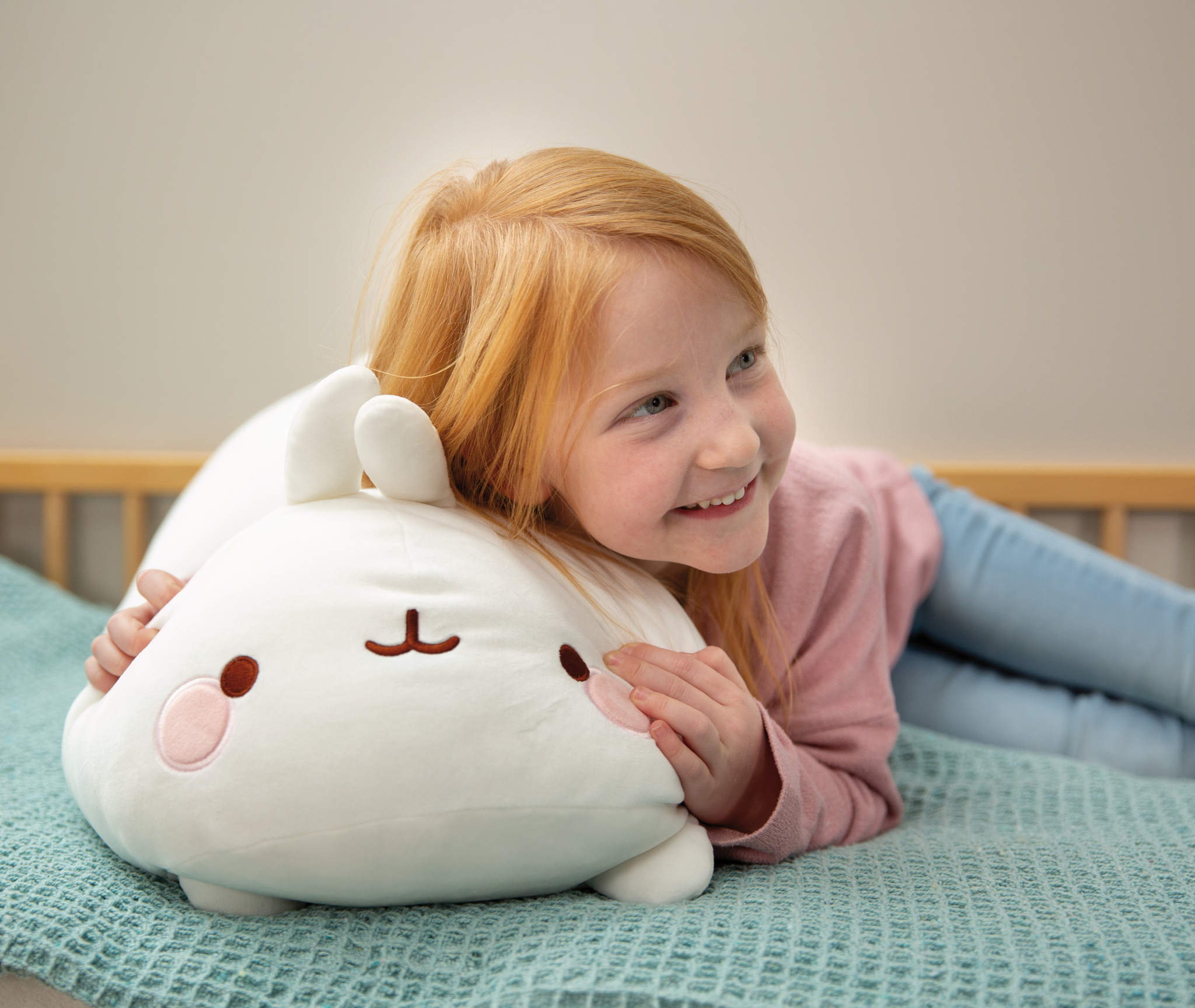 Dziewczyna leży na łóżku, przytulając białą poduszkę w kształcie królika, uśmiechając się do aparatu, w sypialni.