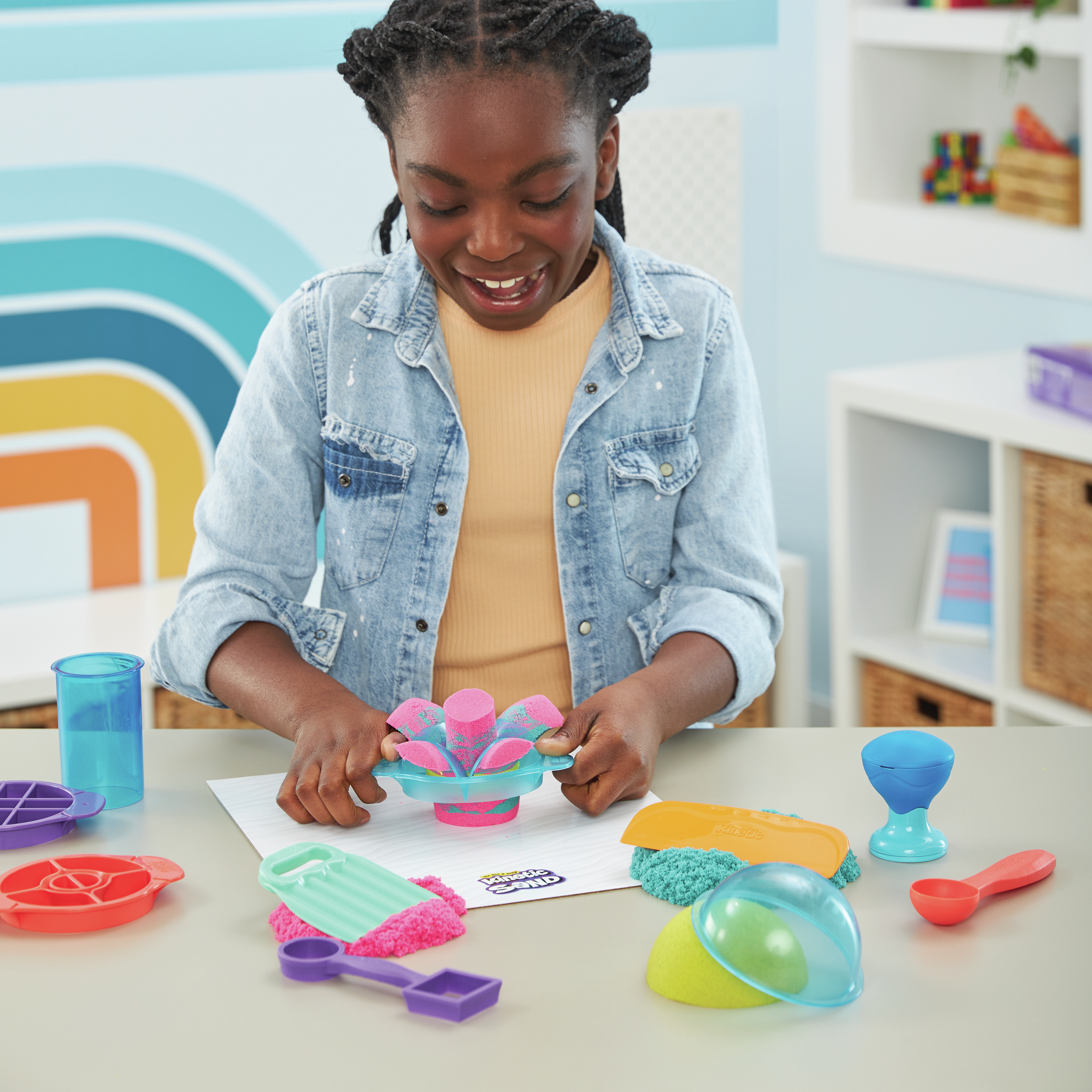 Dziewczyna bawiąca się piaskiem kinetycznym z narzędziami na stole.