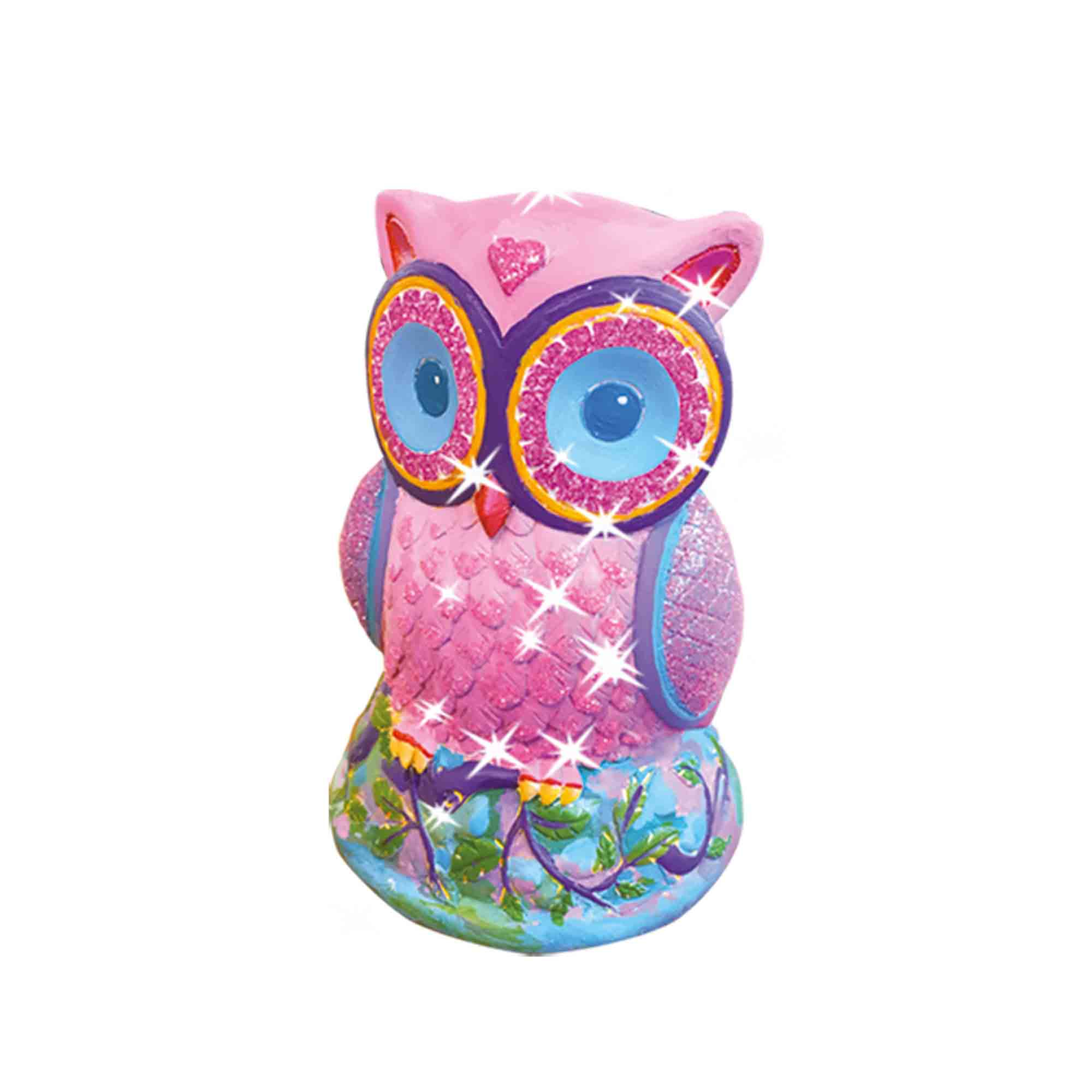 Różowa figurka sowy z brokatem i niebieskimi oczami na podstawie z liśćmi i kwiatami.