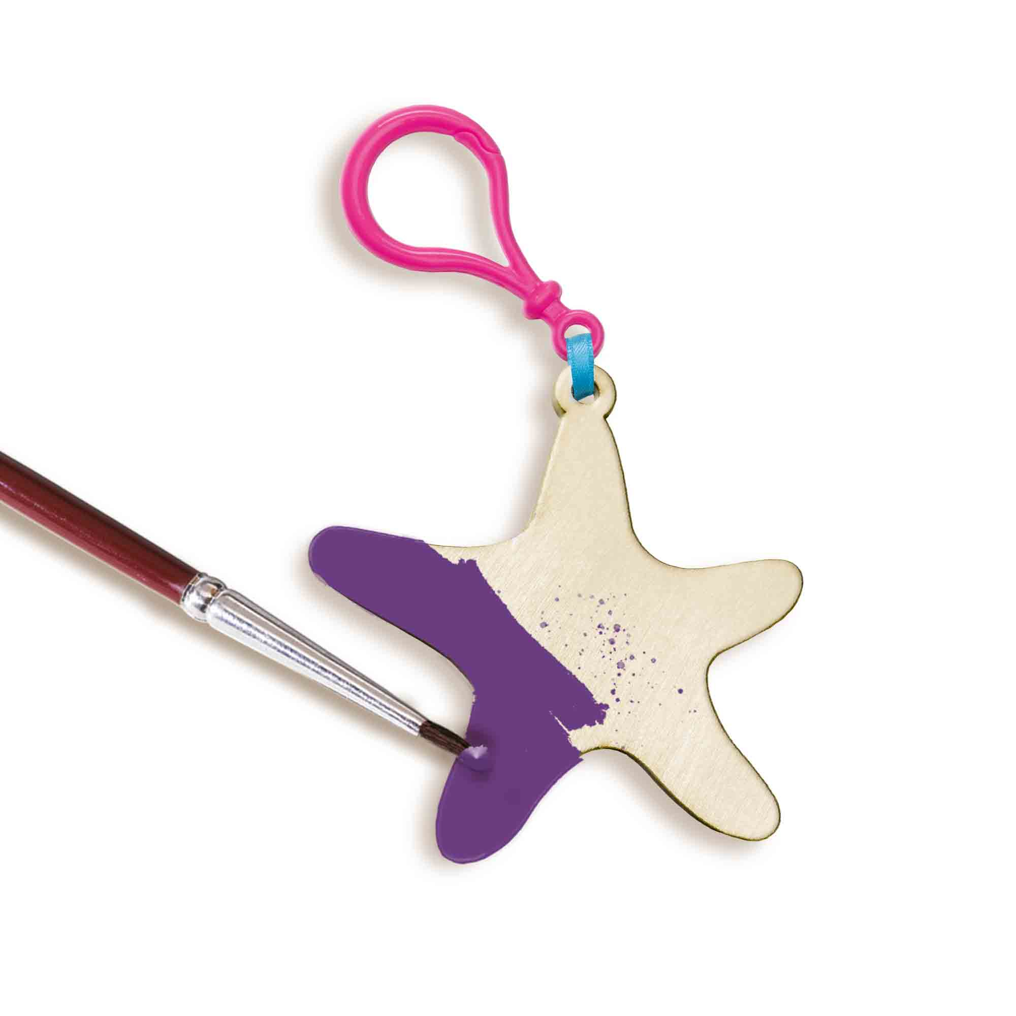Drewniany brelok w kształcie gwiazdy malowany na fioletowo pędzlem, na białym tle.