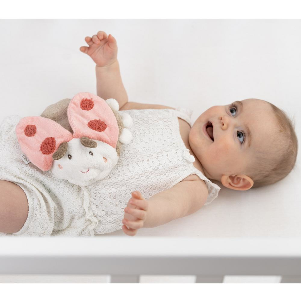 Niemowlę leży trzymając zabawkę w kształcie biedronki. Biedronka jest różowa, brązowa i biała.