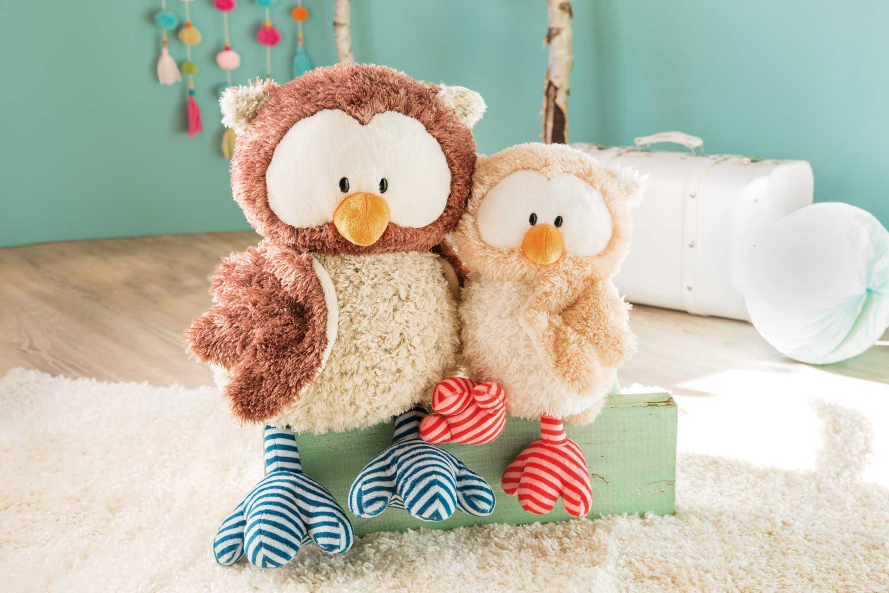 Dwie pluszowe sowy na zielonej powierzchni z jasnym tłem.