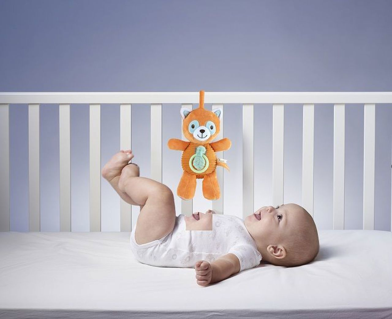 Ein Baby liegt im Kinderbett und schaut auf ein hängendes Orangenspielzeug.