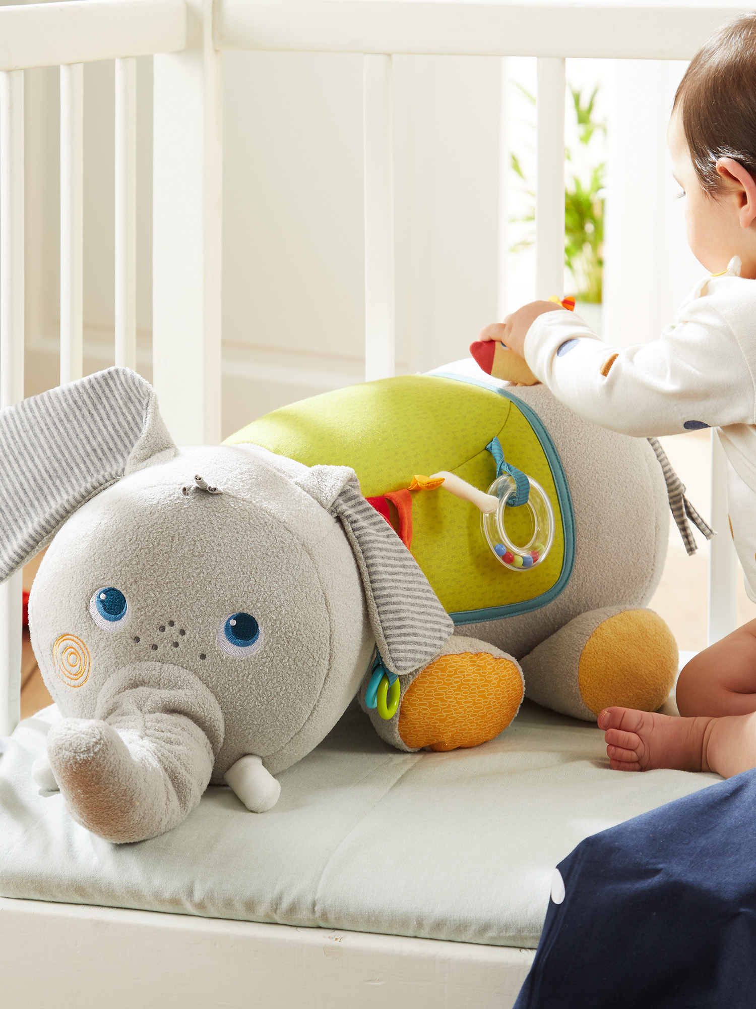 Baby spielt mit einem Elefanten-Plüschtier in einem Kinderbett. Verschwommener Hintergrund.