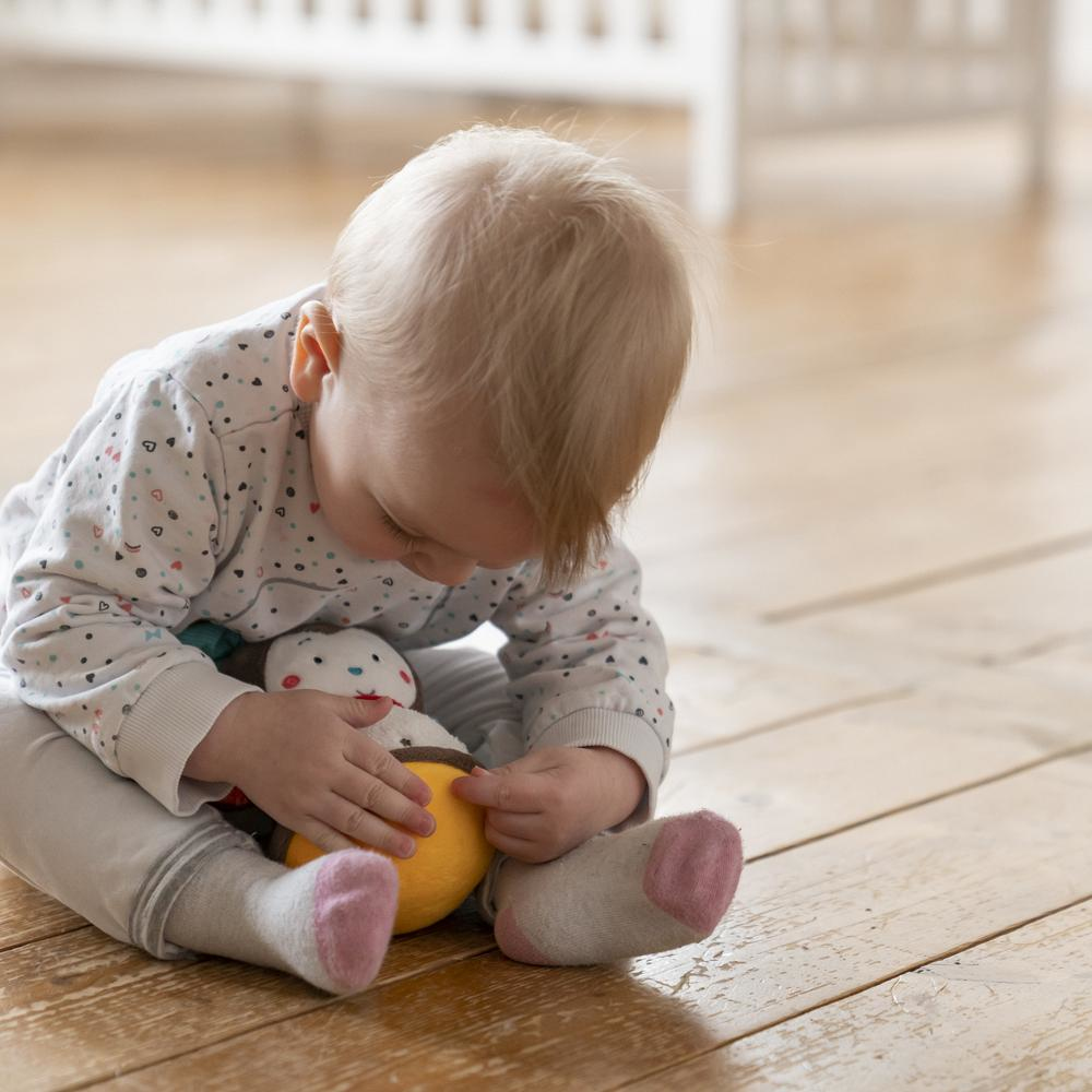 Niemowlę bawi się zabawką na drewnianej podłodze.