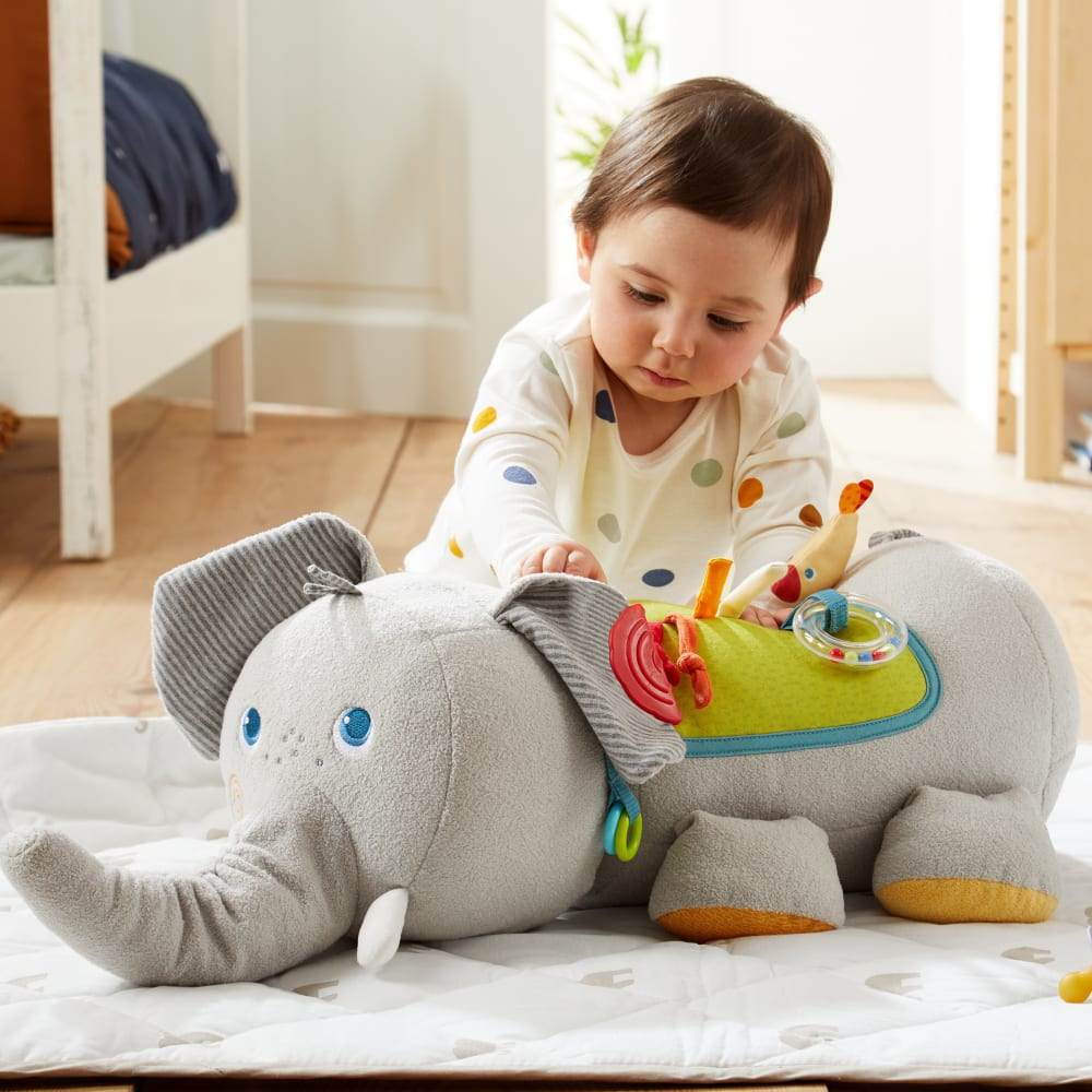 Ein Baby spielt mit einem Elefantenspielzeug auf einer Spielmatte in einem Schlafzimmer.