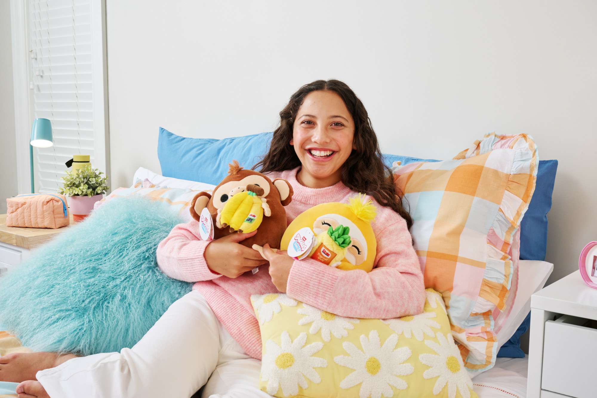 Teenager lächelt und hält zwei Plüschtiere auf einem Bett.
