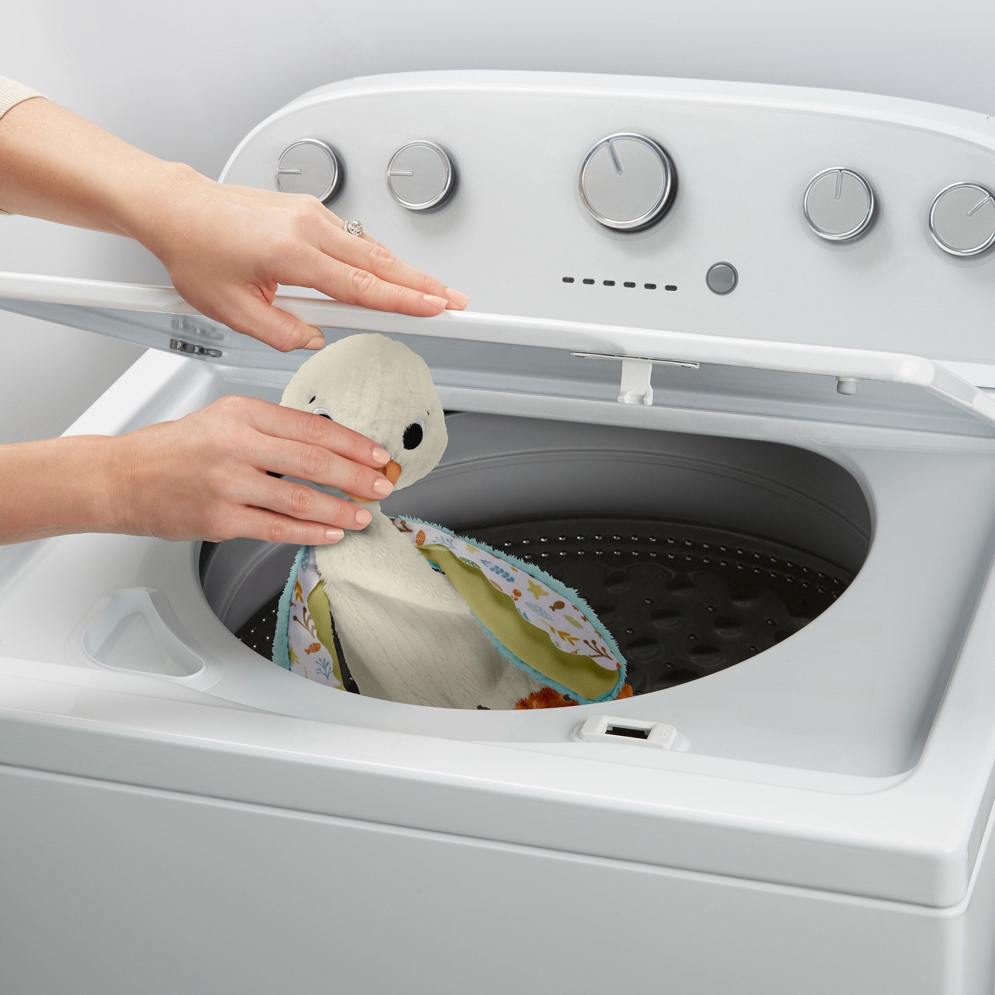 Ręce wkładają białą pluszową kaczkę do białej pralki.