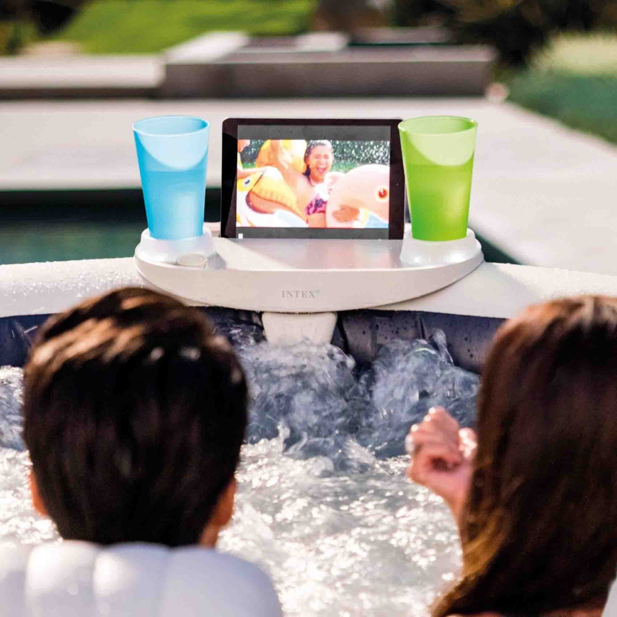 Ludzie w jacuzzi oglądają tablet. Dwa szklanki stoją na tacy, jedna niebieska i jedna zielona.