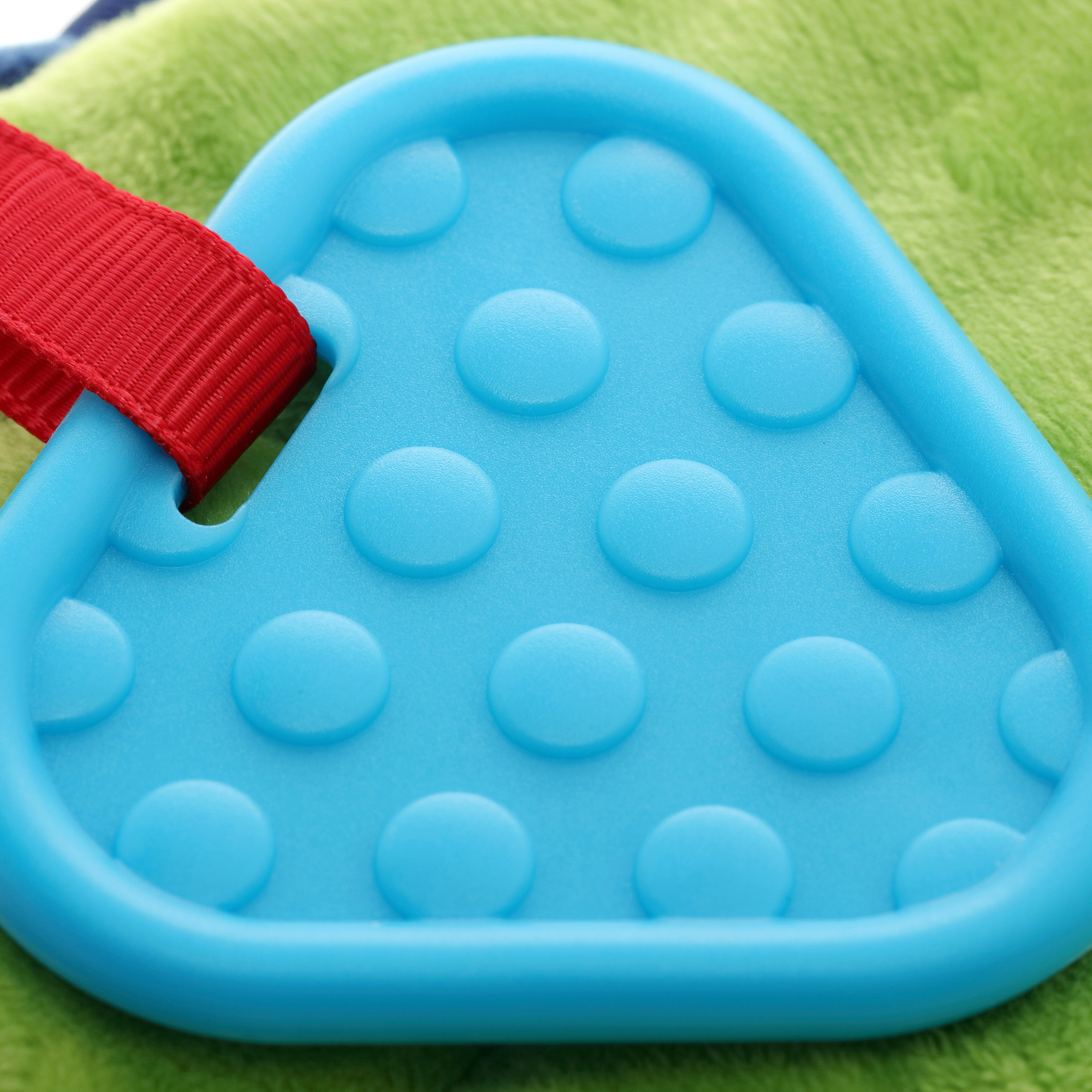 Zbliżenie niebieskiej zabawki do gryzienia z wypukłymi kropkami, przymocowanej do czerwonego paska.
