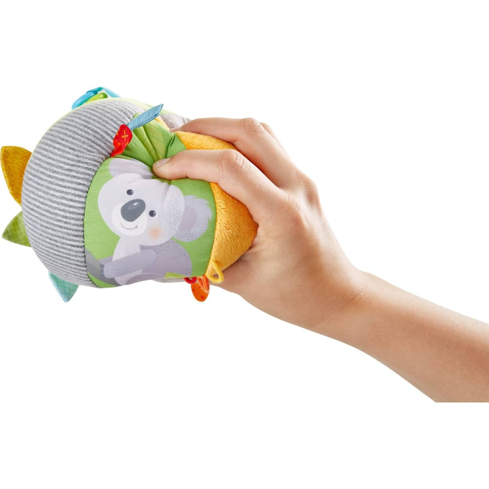 Una mano che tiene una palla per bambini, con un'illustrazione di koala. Varie sezioni di tessuto colorate.
