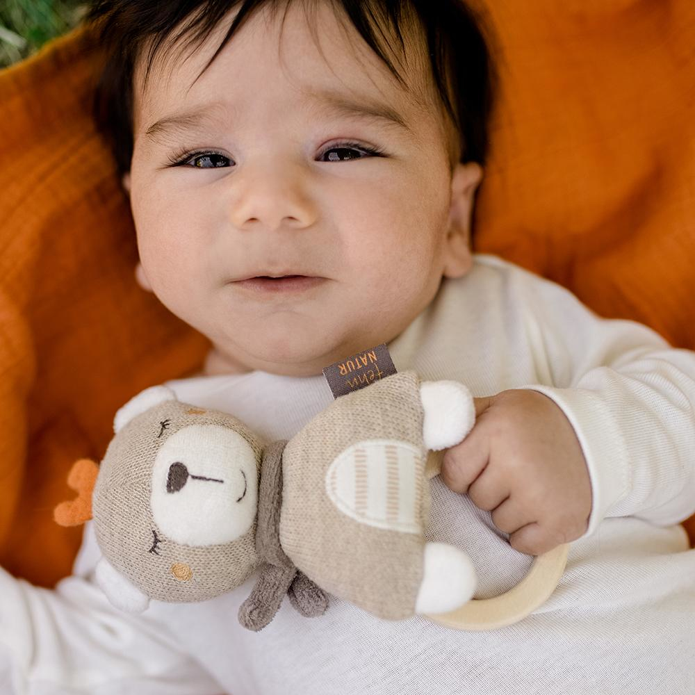 Primo piano di un bambino che tiene in mano un giocattolo a forma di orso. Il bambino è sdraiato su una coperta arancione.