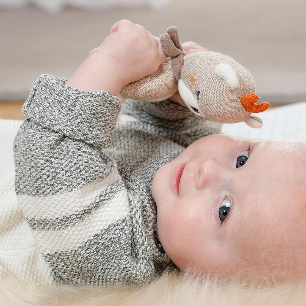 Bambino sdraiato, che tiene in mano un giocattolo a forma di cervo. Il bambino ha la pelle chiara.