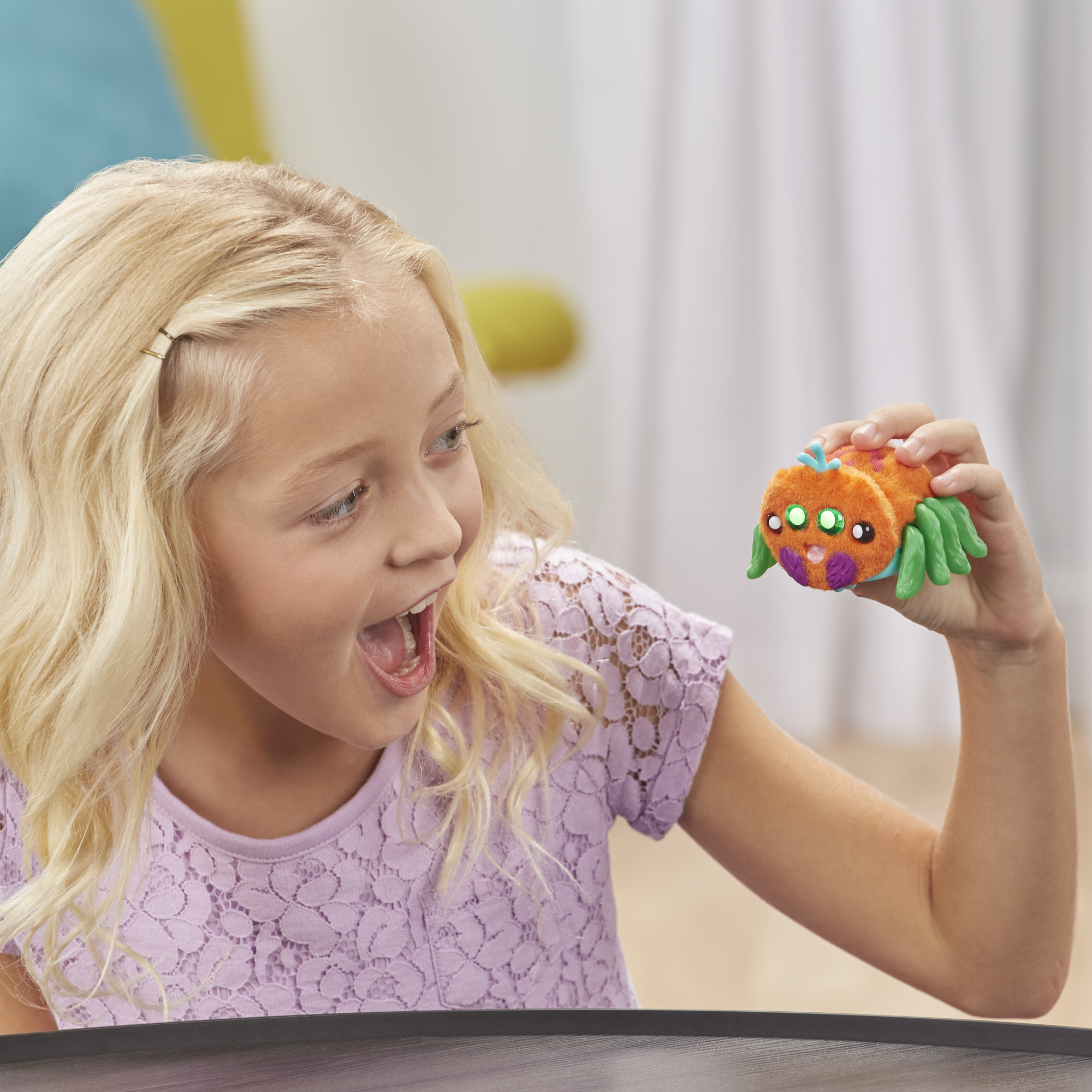 Blondes Mädchen hält aufgeregt eine orangefarbene Spielzeugspinne und schaut sie mit offenem Mund an.