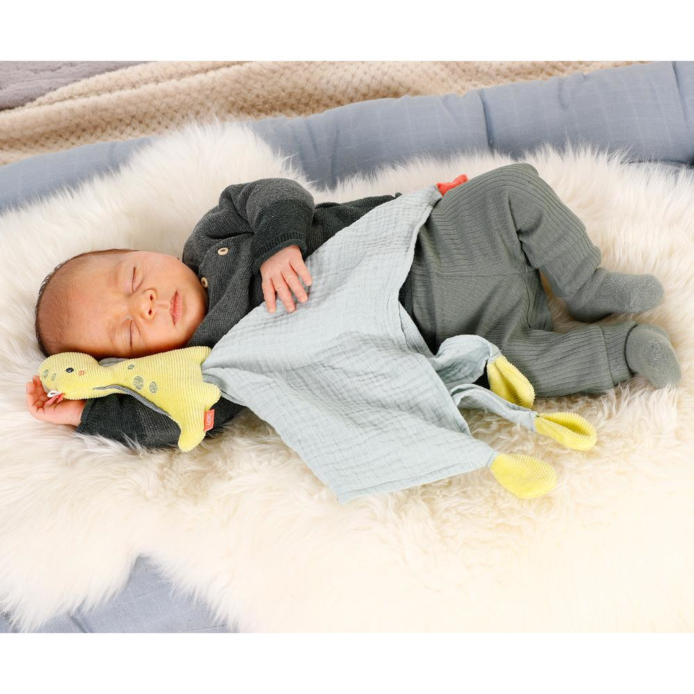 Śpiące dziecko leżące na futrzanym dywanie, z zabawką i kocykiem.