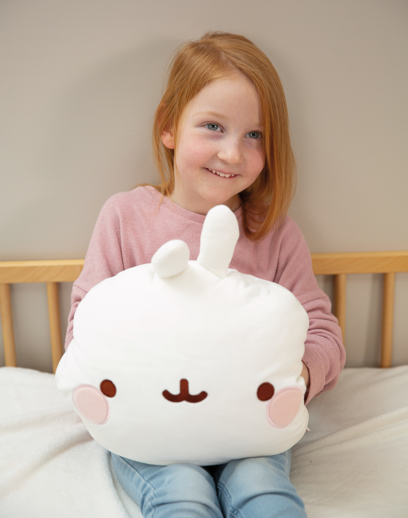 Uśmiechnięta dziewczyna trzymająca białą poduszkę w kształcie królika z różowymi policzkami i uśmiechniętą twarzą.