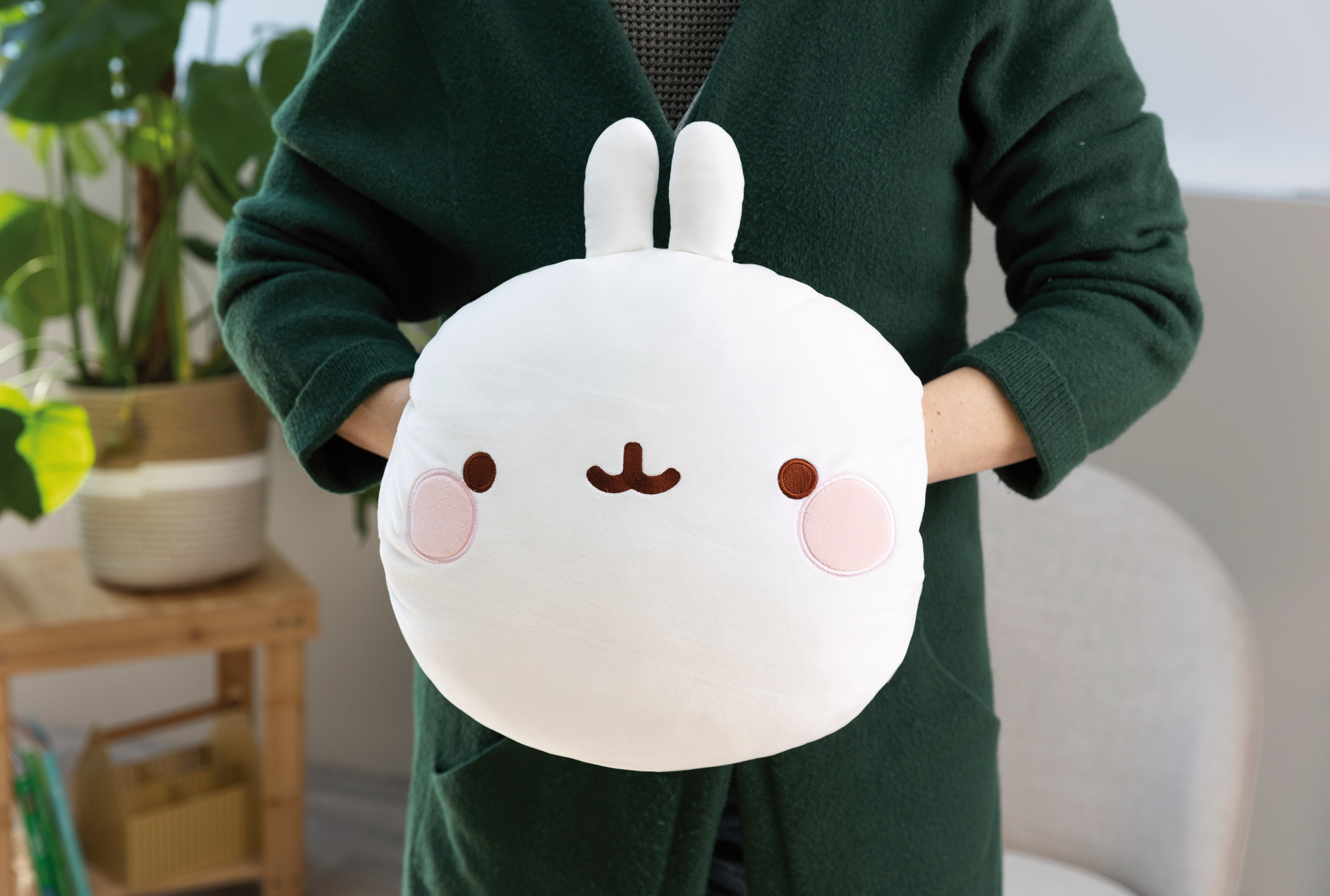 Osoba trzyma białą pluszową zabawkę z twarzą, różowymi policzkami.