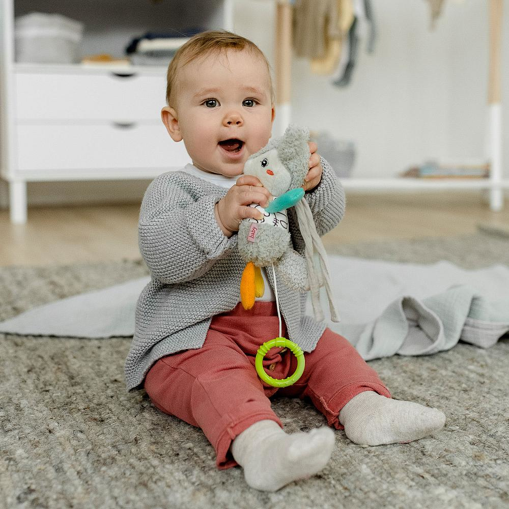Un bambino seduto, tiene un peluche e guarda la fotocamera con un sorriso.