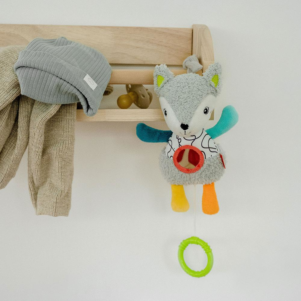 Un peluche a forma di volpe, appeso a una mensola di legno. Accanto un cappello e una sciarpa.