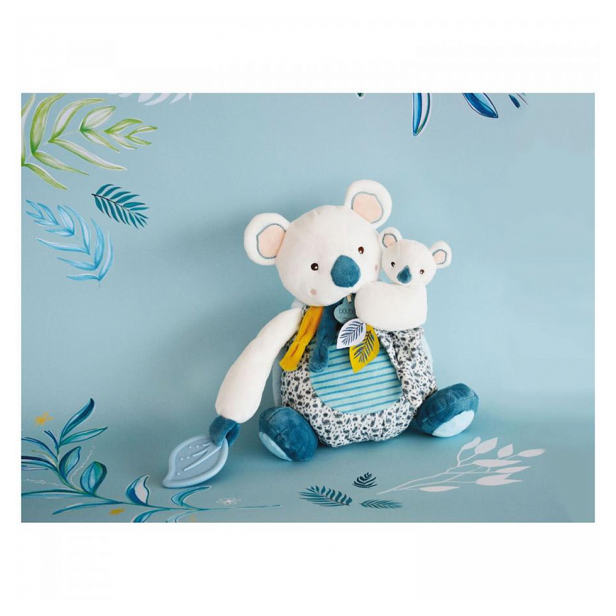 Un peluche a forma di koala con un cucciolo di koala sulla schiena. Sono su uno sfondo blu con foglie.