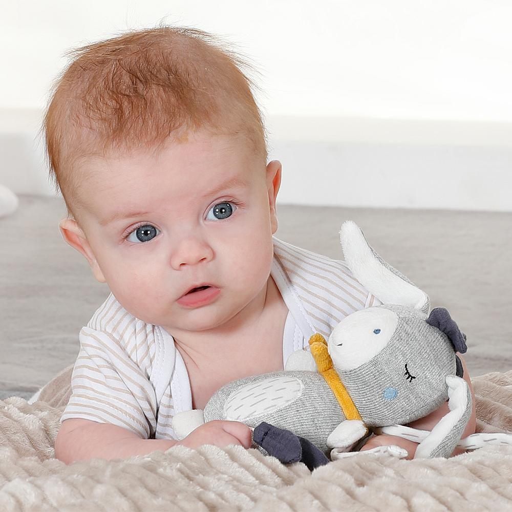 Baby mit grauem Hasen-Plüschtier. Baby liegt auf einer Decke und schaut in die Kamera.