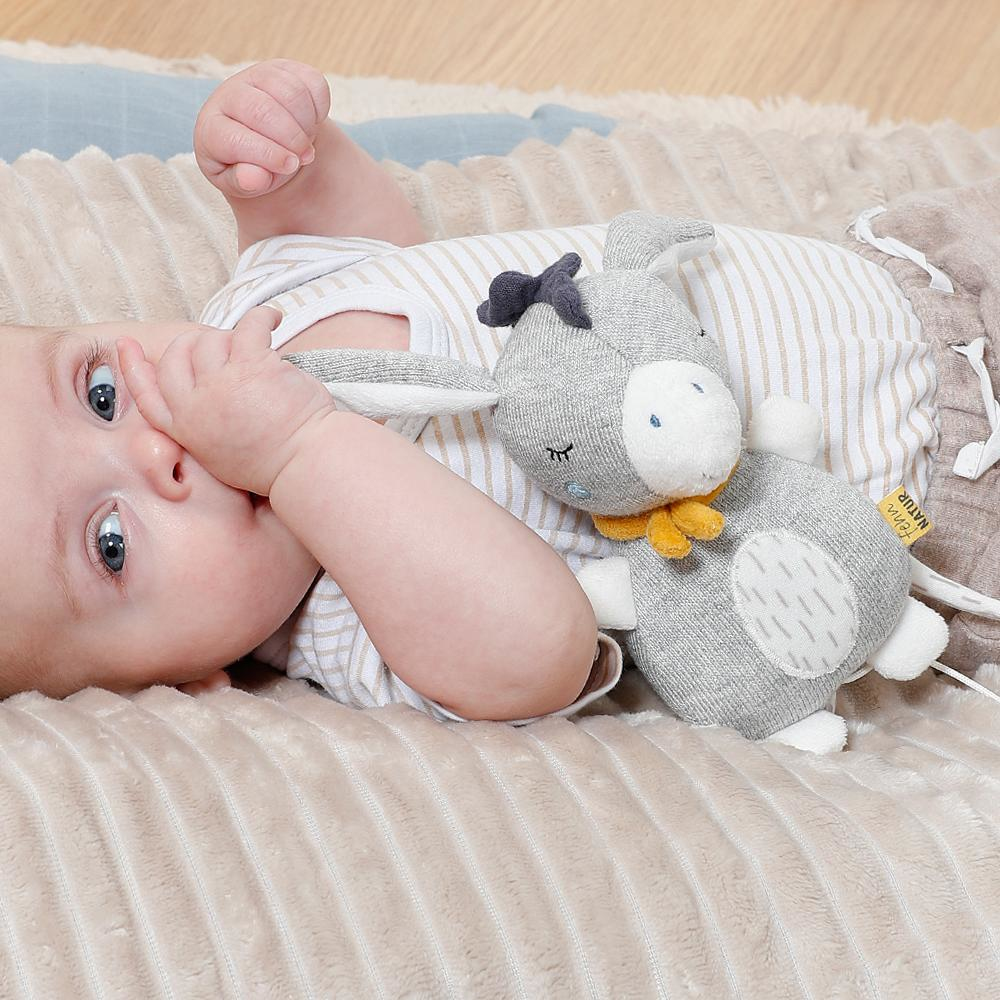 Baby auf einer Decke mit einem grauen Hasenplüsch. Baby schaut in die Kamera.