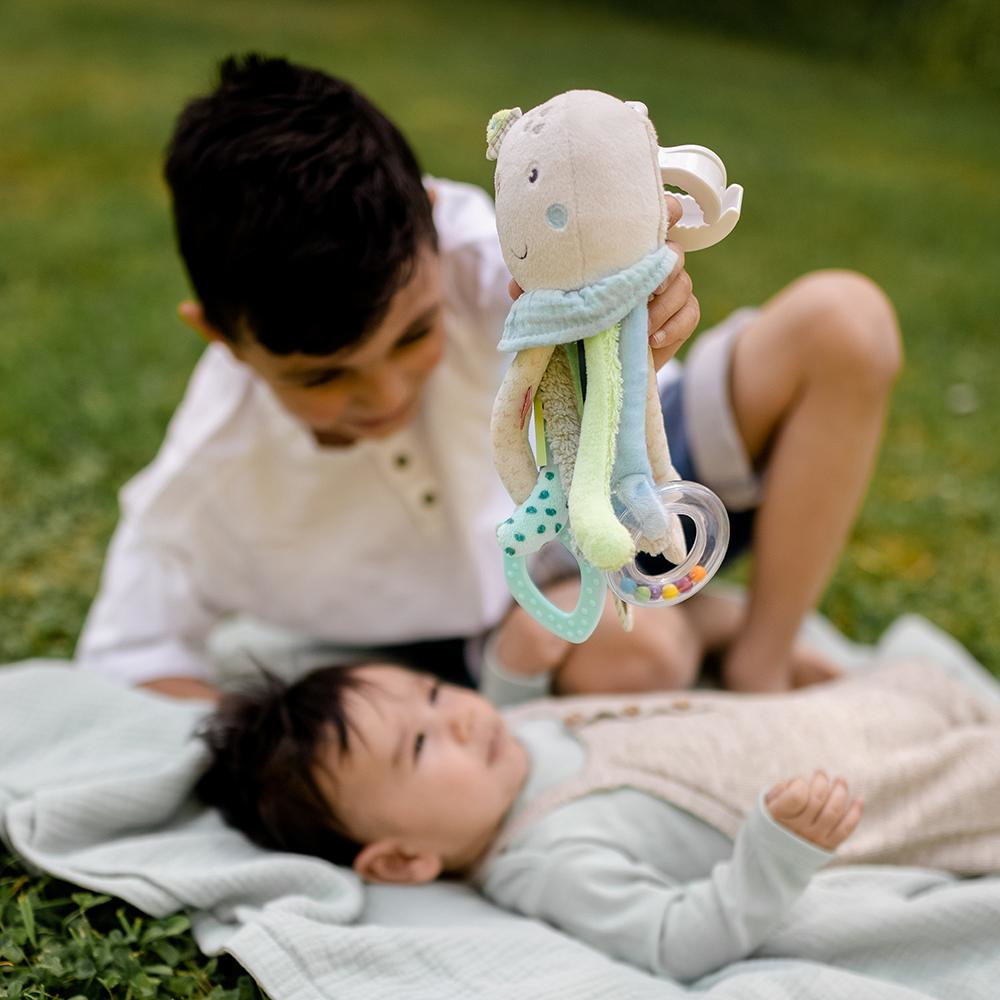 Dwóch chłopców bawi się zabawką ośmiornicą. Jeden ją trzyma, drugi leży na kocu z niemowlęciem.