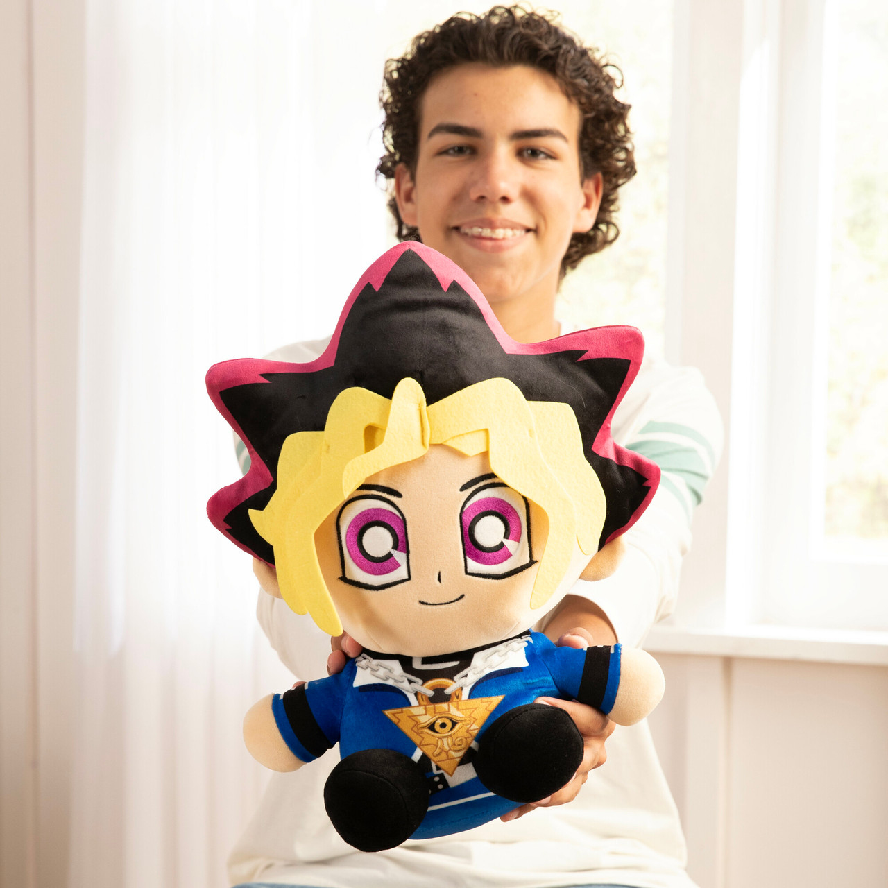 Ein Mann hält ein Yu-Gi-Oh-Plüschtier. Das Spielzeug ist ein Junge mit schwarzen und pinken Haaren, blaue Jacke.
